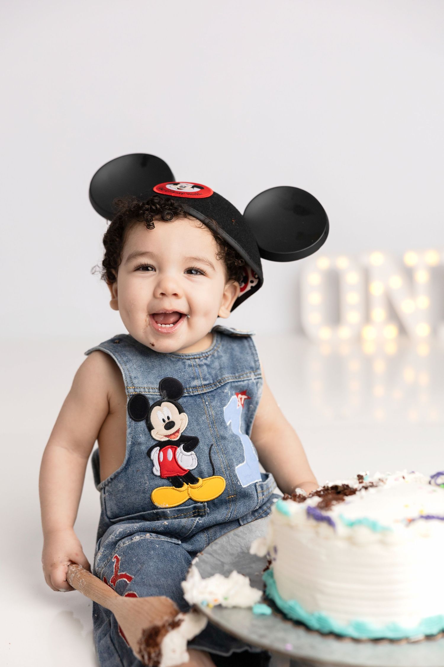Mickey Mouse themed cake smash photo session with denim outfit and mouse ears.