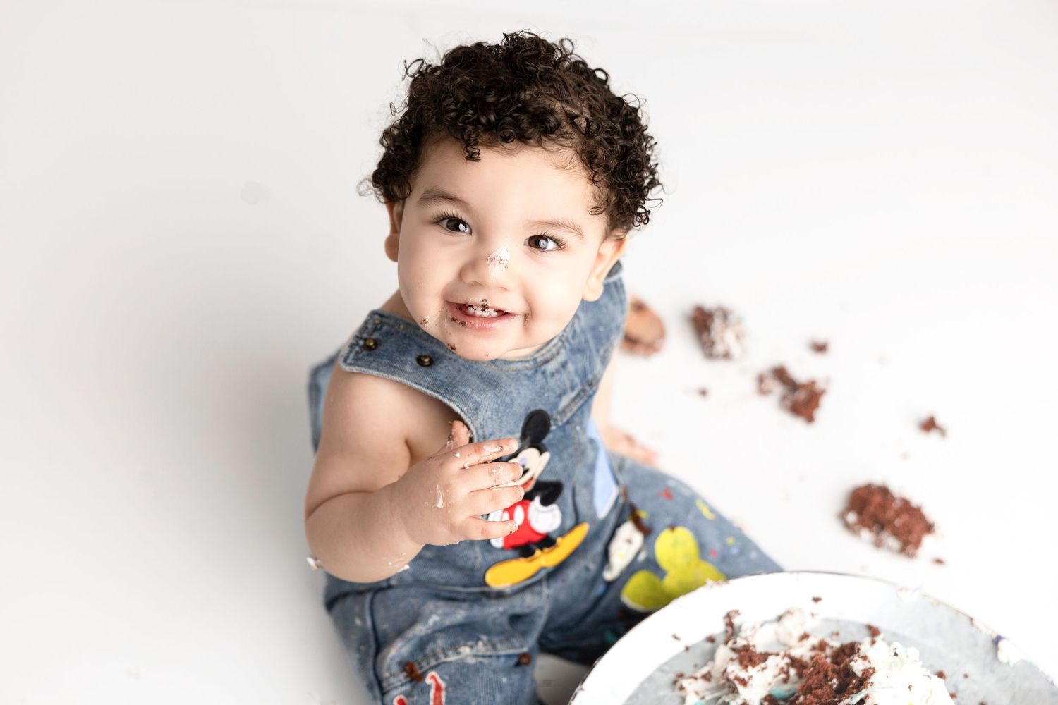 Toddler in Mickey Mouse denim outfit enjoying birthday cake.
