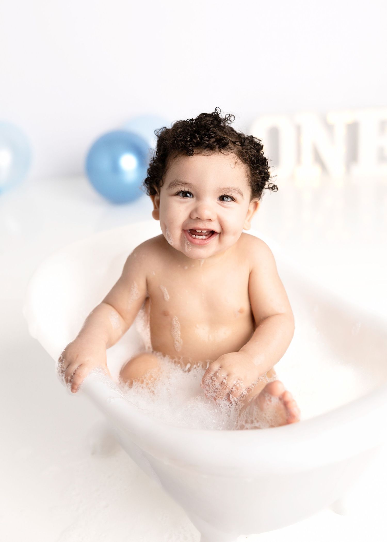 Happy bath time photo shoot with bubbles and blue balloons in background.