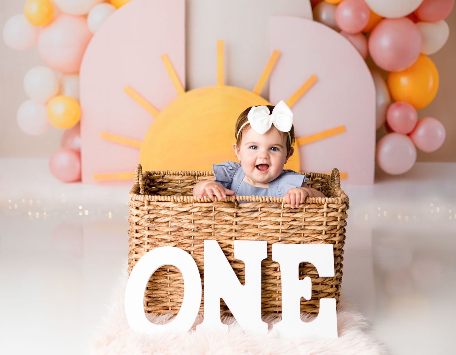 First birthday setup with wicker basket and balloon arch in pink and orange.