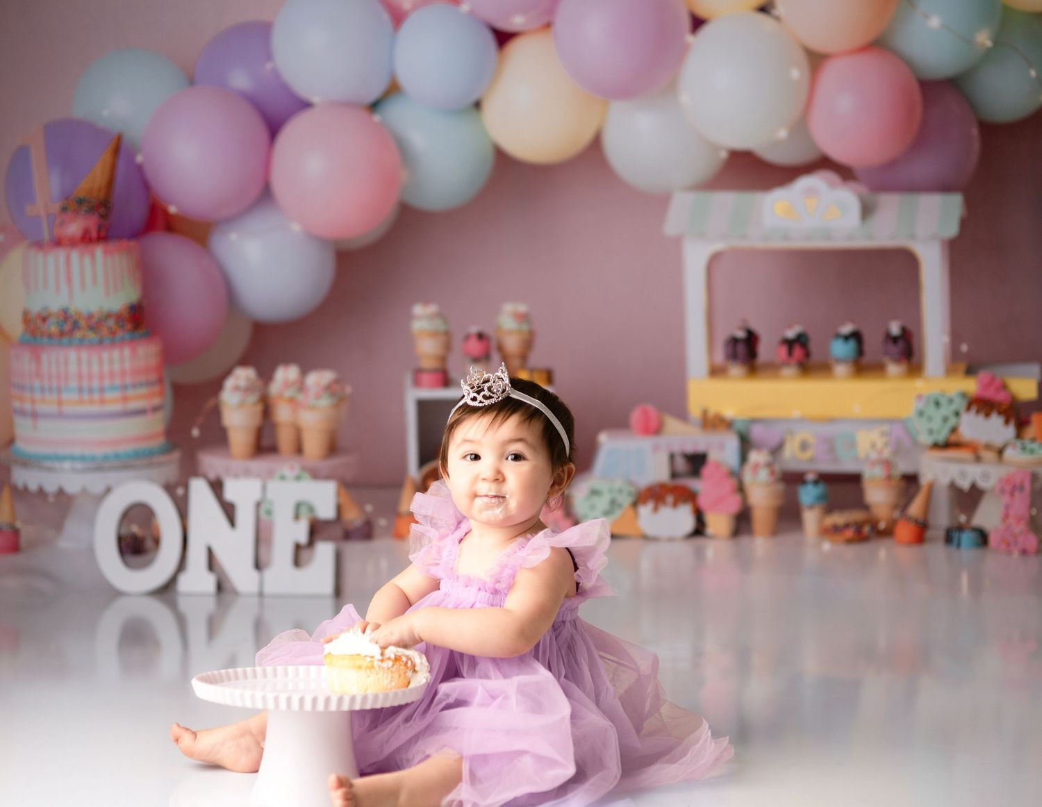First birthday party scene with pink balloon arch and pastel decorations.