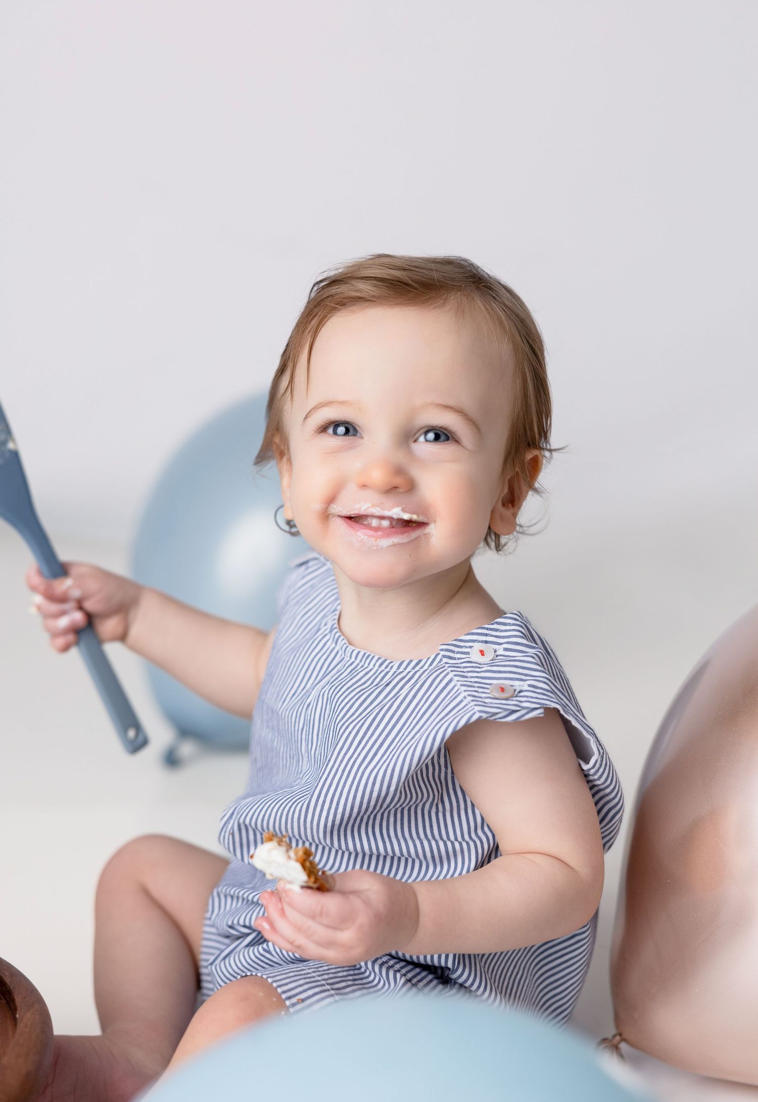 Happy baby in blue striped outfit reaching for cake during photoshoot.