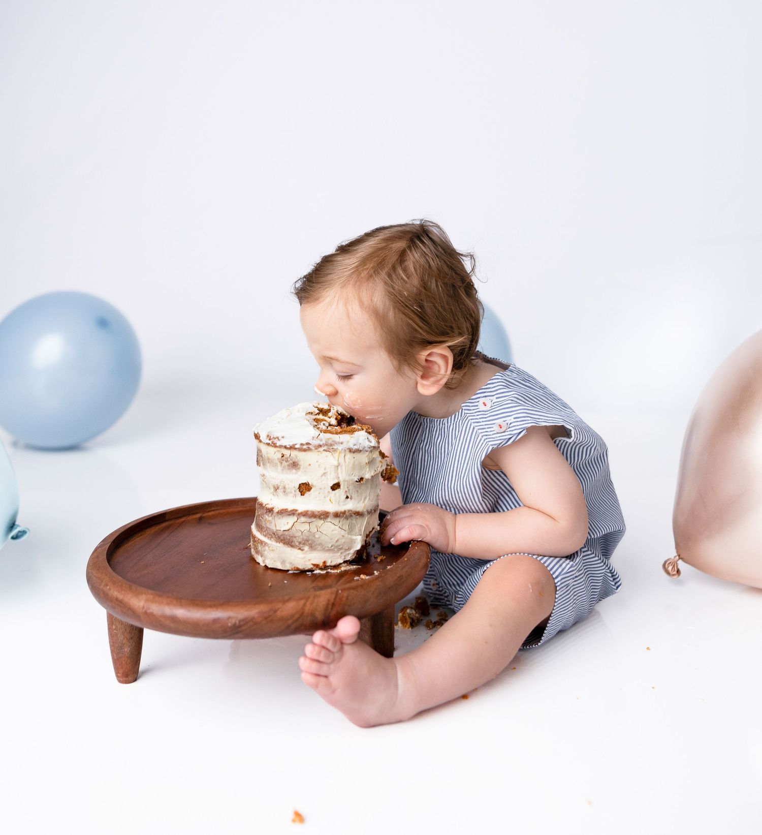 Baby exploring cake during first birthday photoshoot with blue balloon decor.