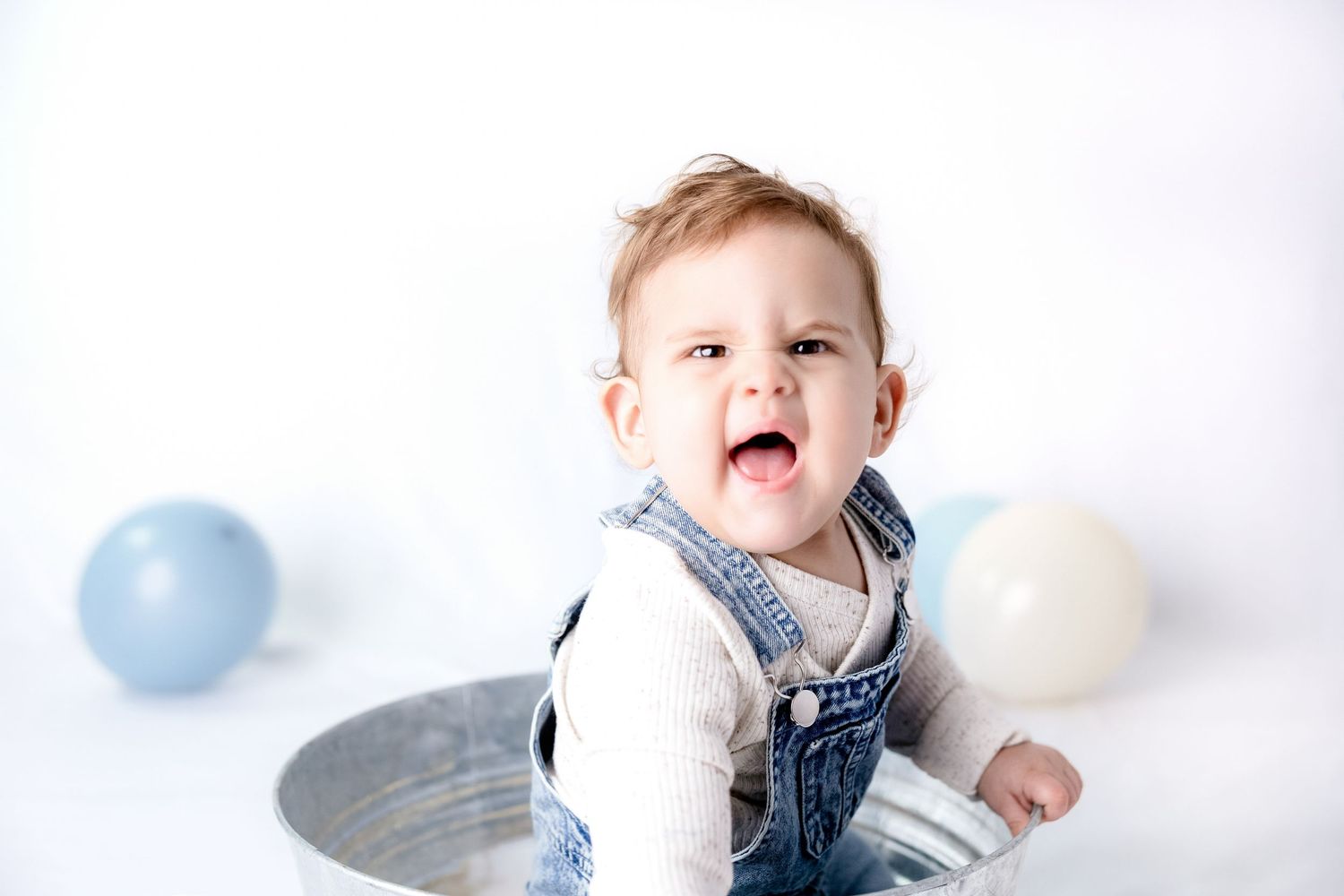 Baby in denim overalls plays with blue and white decorations in studio setting.