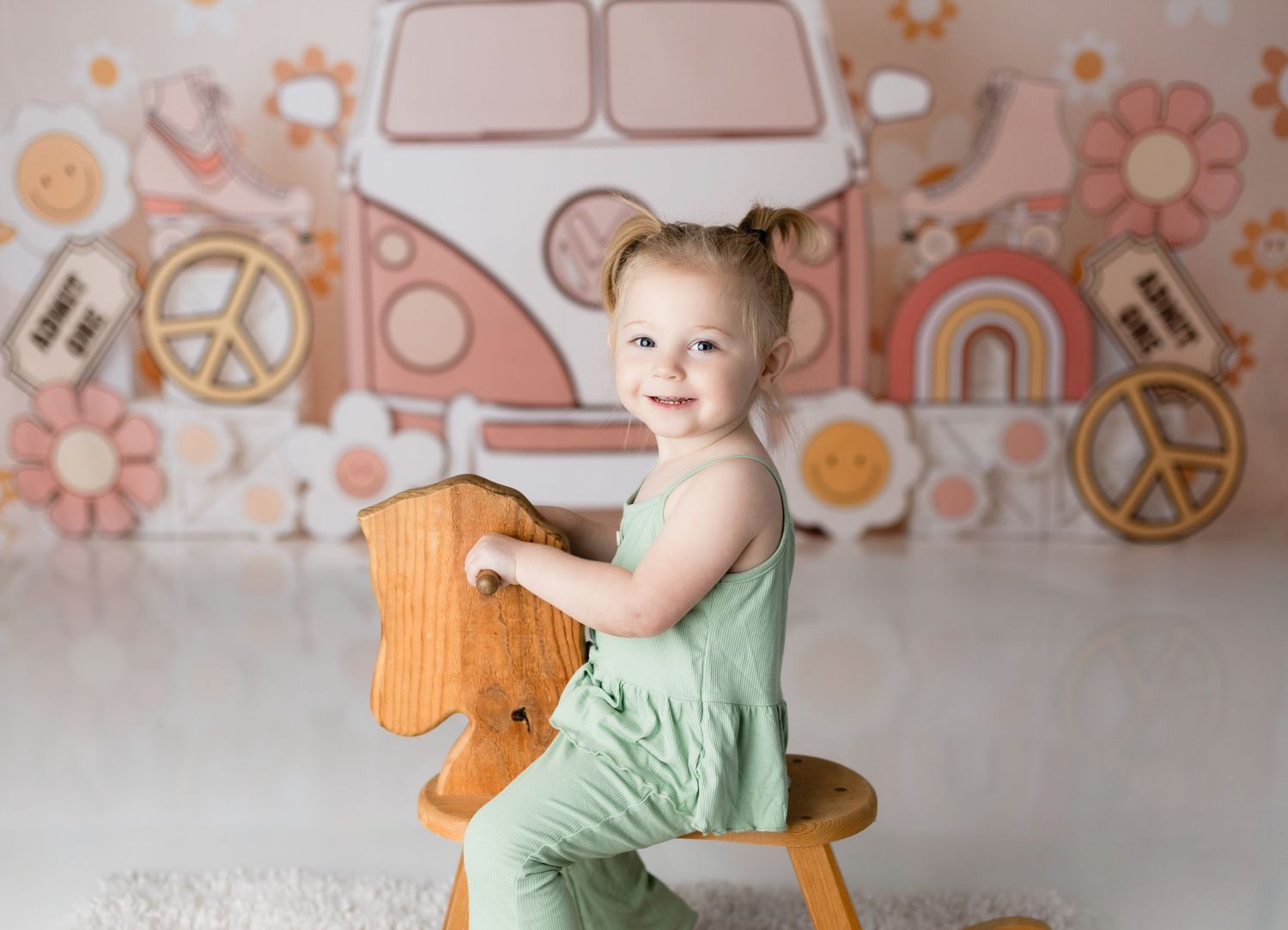 Toddler in mint green outfit riding wooden rocking horse against retro van backdrop.