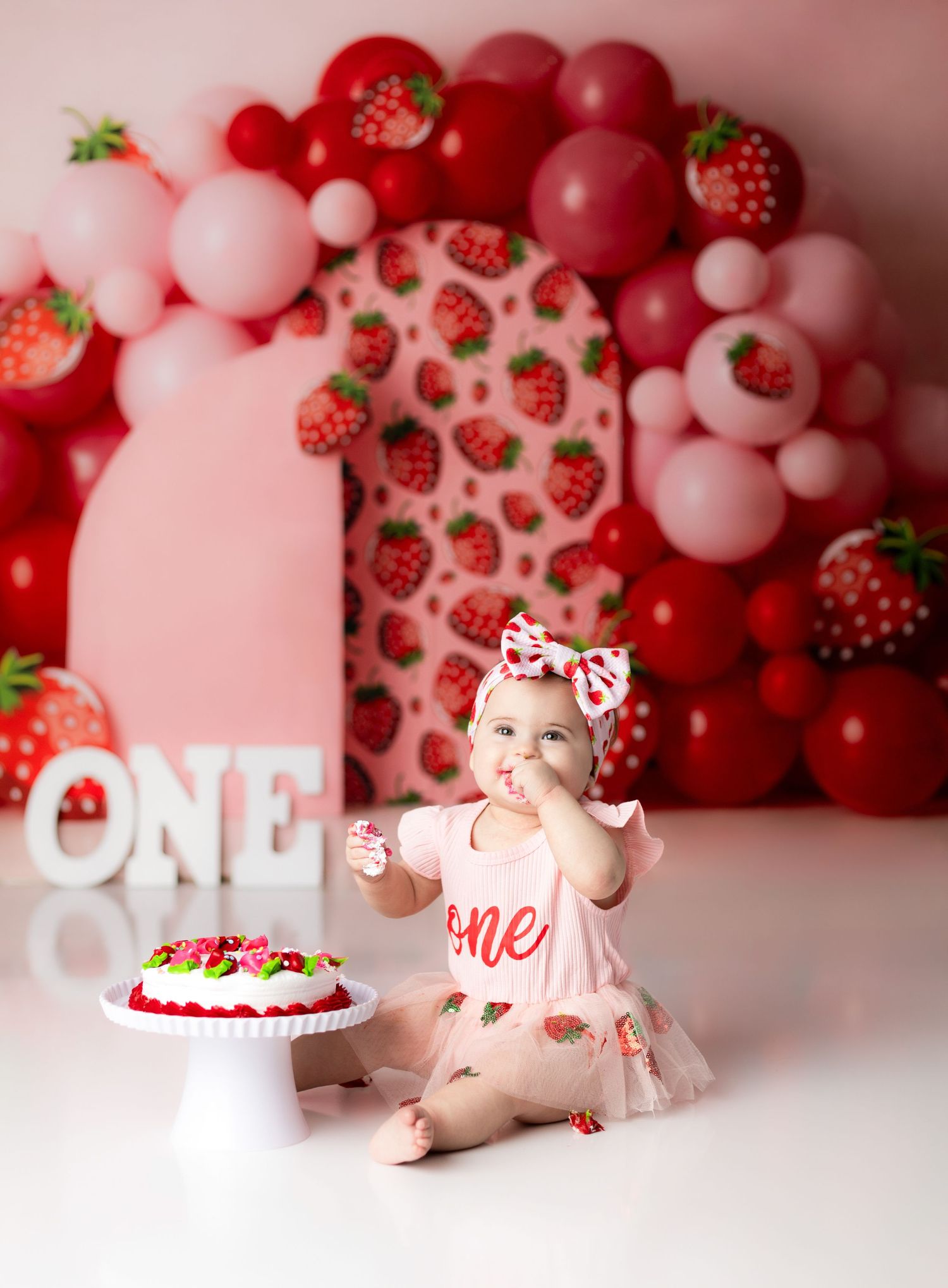 Strawberry themed first birthday setup with cake, balloons, and pink decorations.