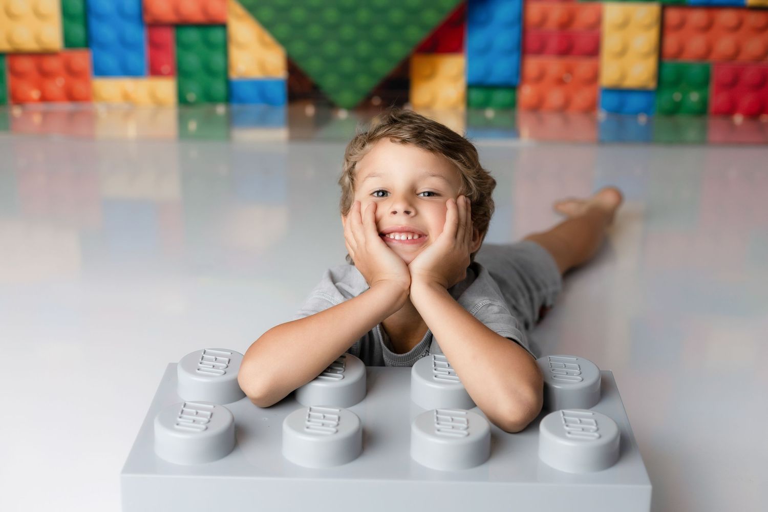 Child playing peek-a-boo with hands covering eyes against colorful LEGO block background.