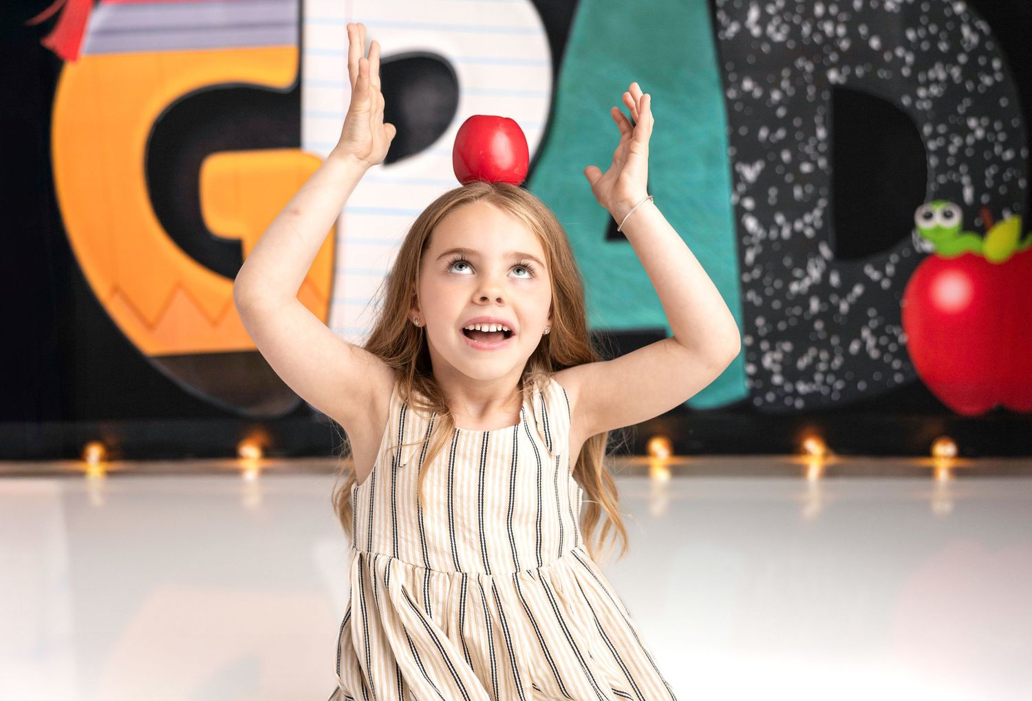 A young graduate in striped dress poses joyfully against a decorated chalkboard.