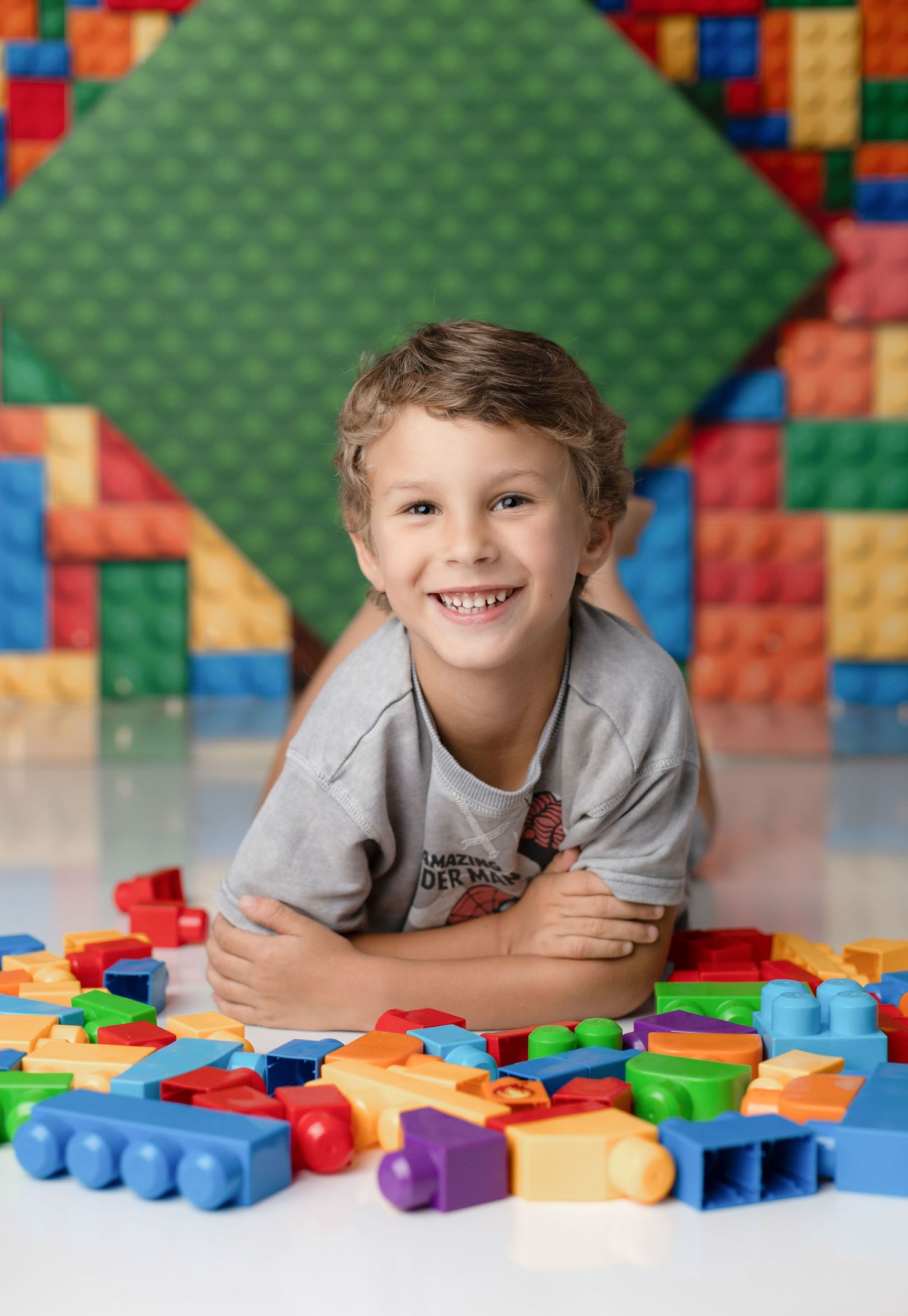 Child playing with colorful LEGO blocks on white surface with green backdrop.