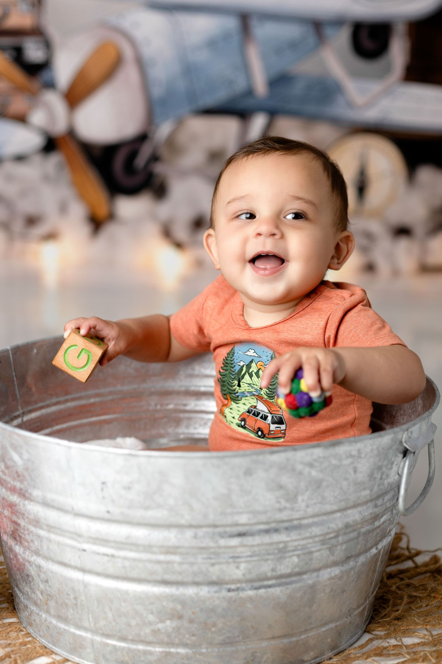 Baby sitting in galvanized metal tub with playful expression.