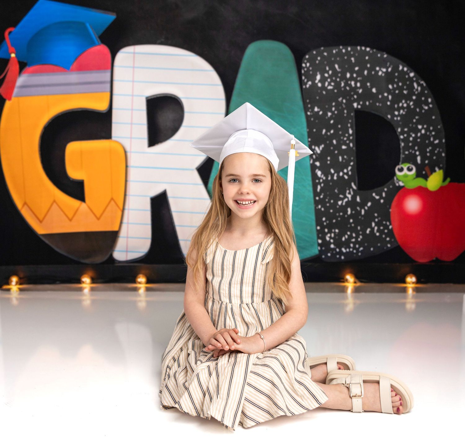 A student celebrates graduation with playful poses against a decorated chalkboard backdrop.