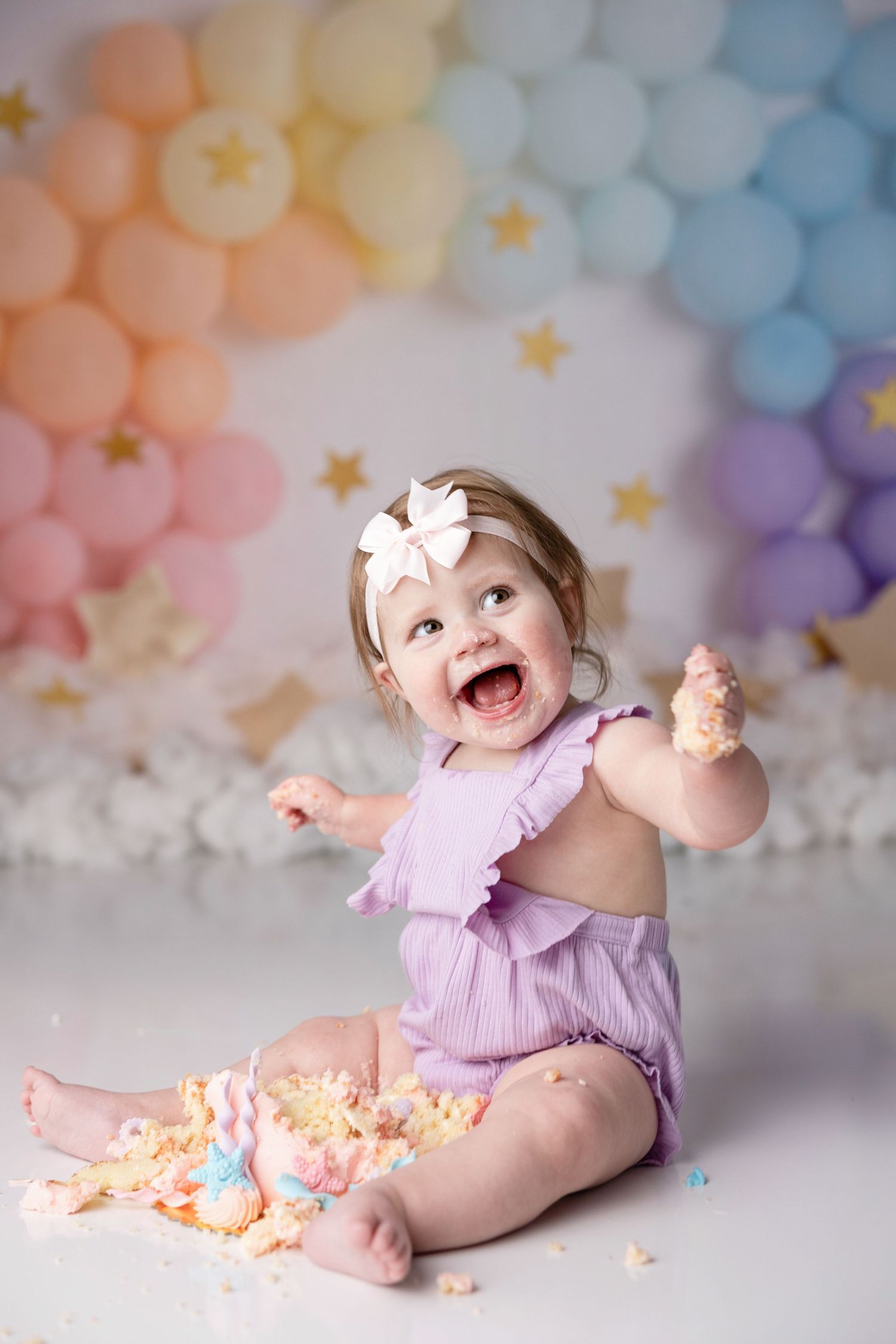 Baby in purple outfit playing with cake during first birthday photoshoot.