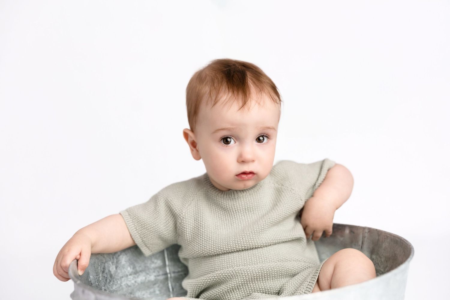 A baby in sage green clothing crawls on a white background.