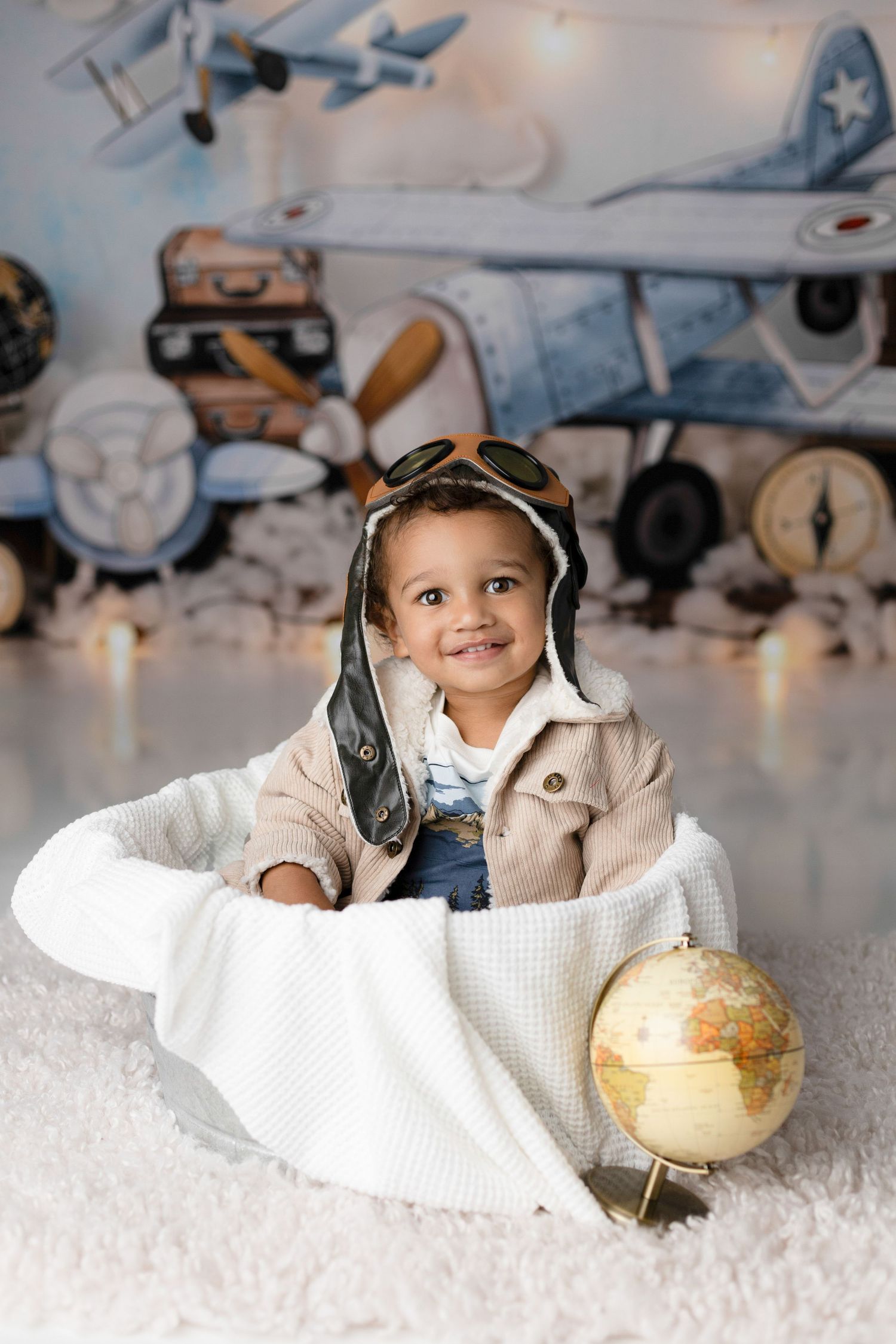 Aviation themed baby photoshoot with globe and white blanket setting.