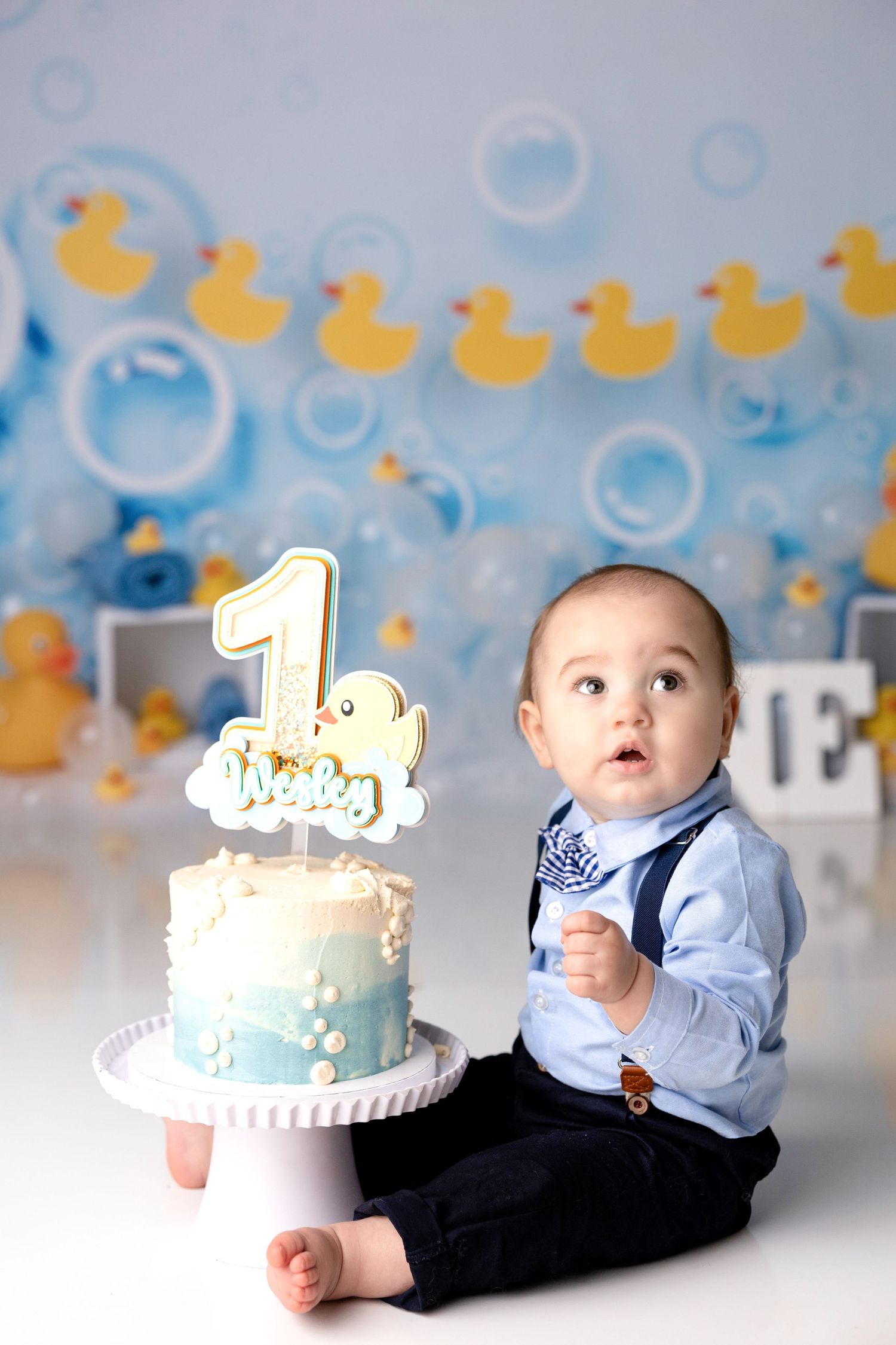 First birthday cake smash setup with rubber duck theme and blue bubbles background.