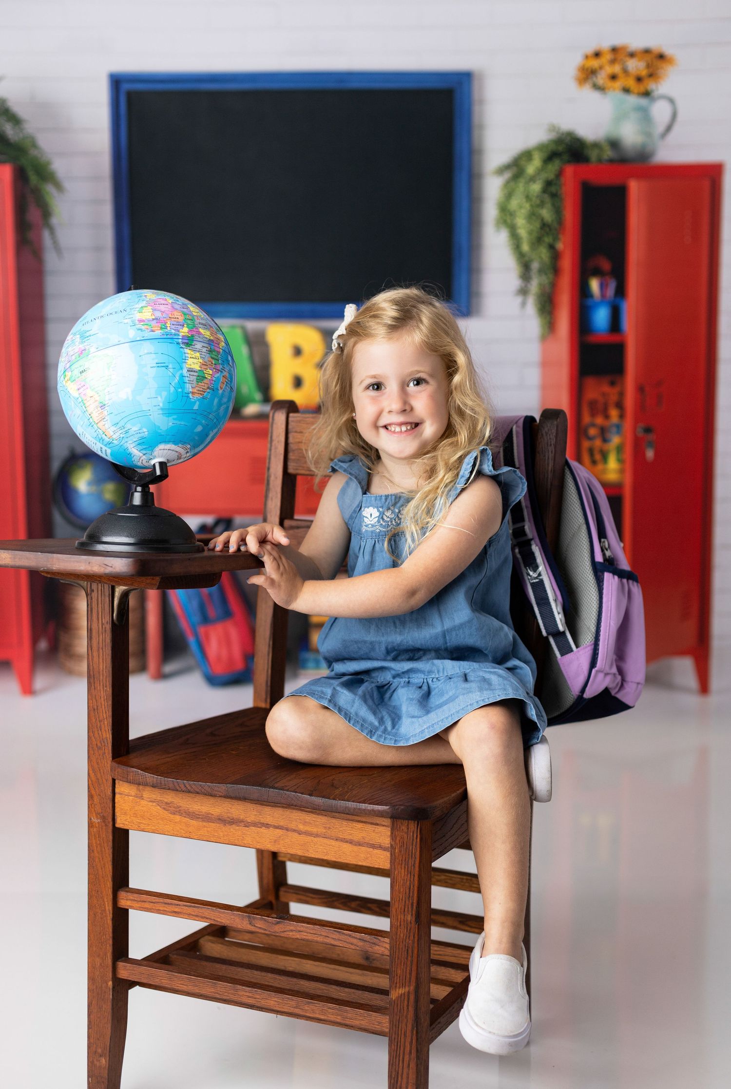 Young student sits on wooden chair with globe in colorful classroom setting.