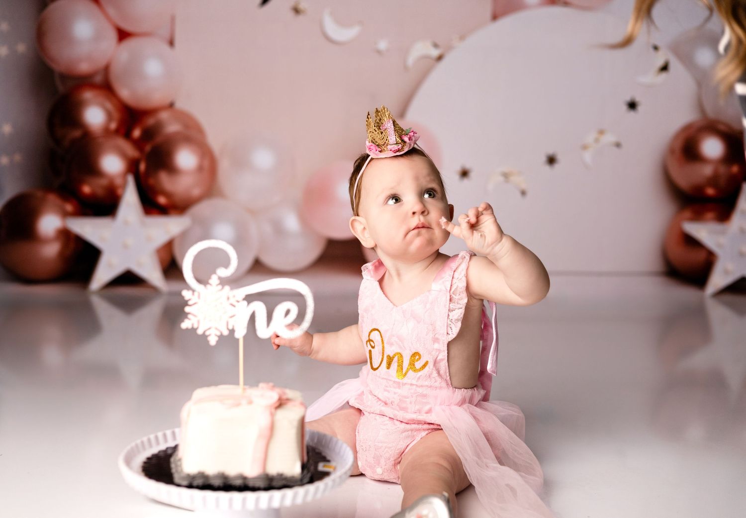Baby in pink tutu dress celebrating first birthday with white cake.