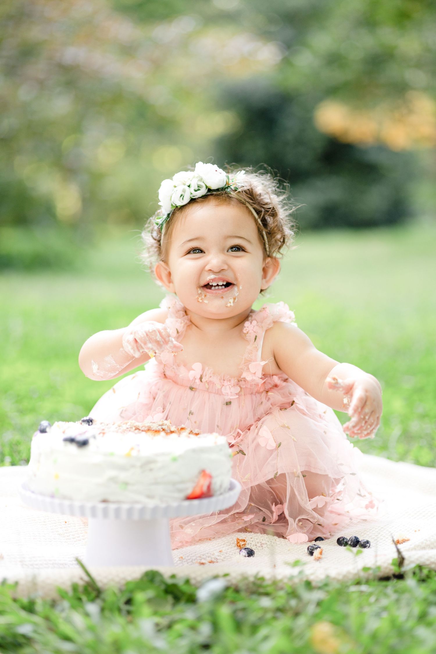 Baby in pink tulle dress enjoying cake smash photoshoot in outdoor garden setting.