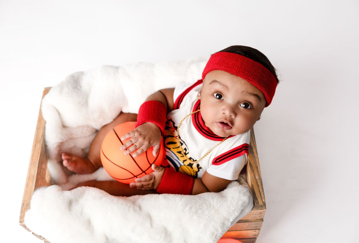 Baby in red and white baseball attire poses on white backdrop.