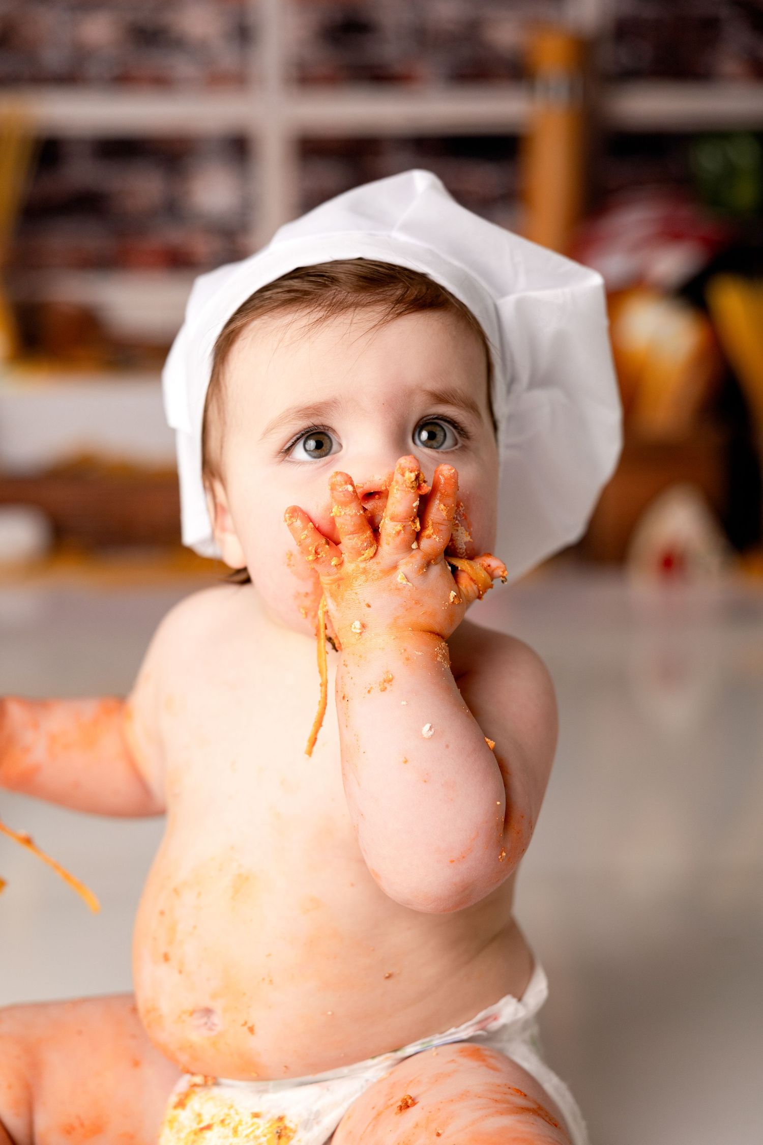 Baby in chef hat gets covered in spaghetti sauce during messy food photoshoot.
