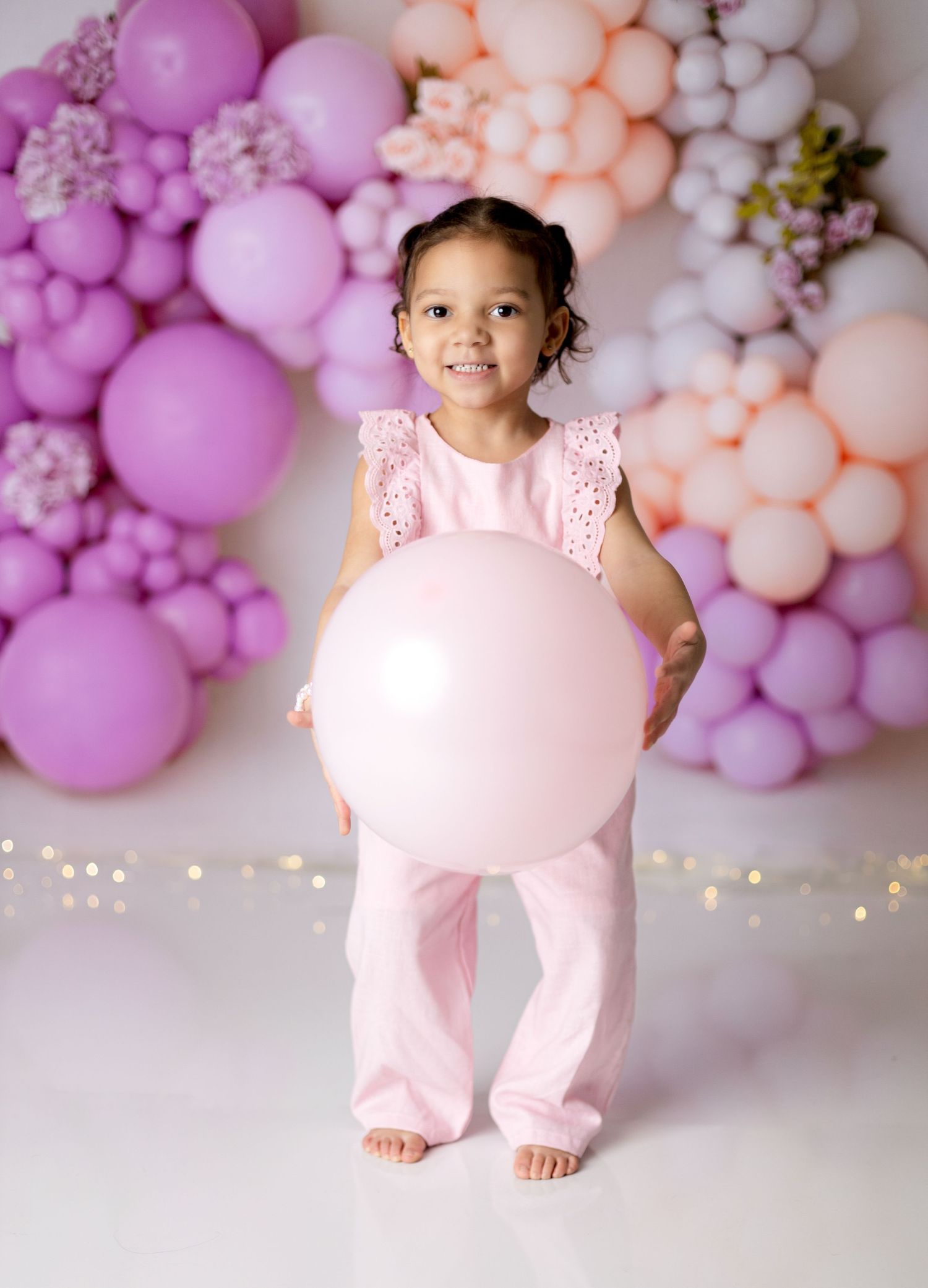 Pink and purple balloon arch backdrop with decorative lighting.