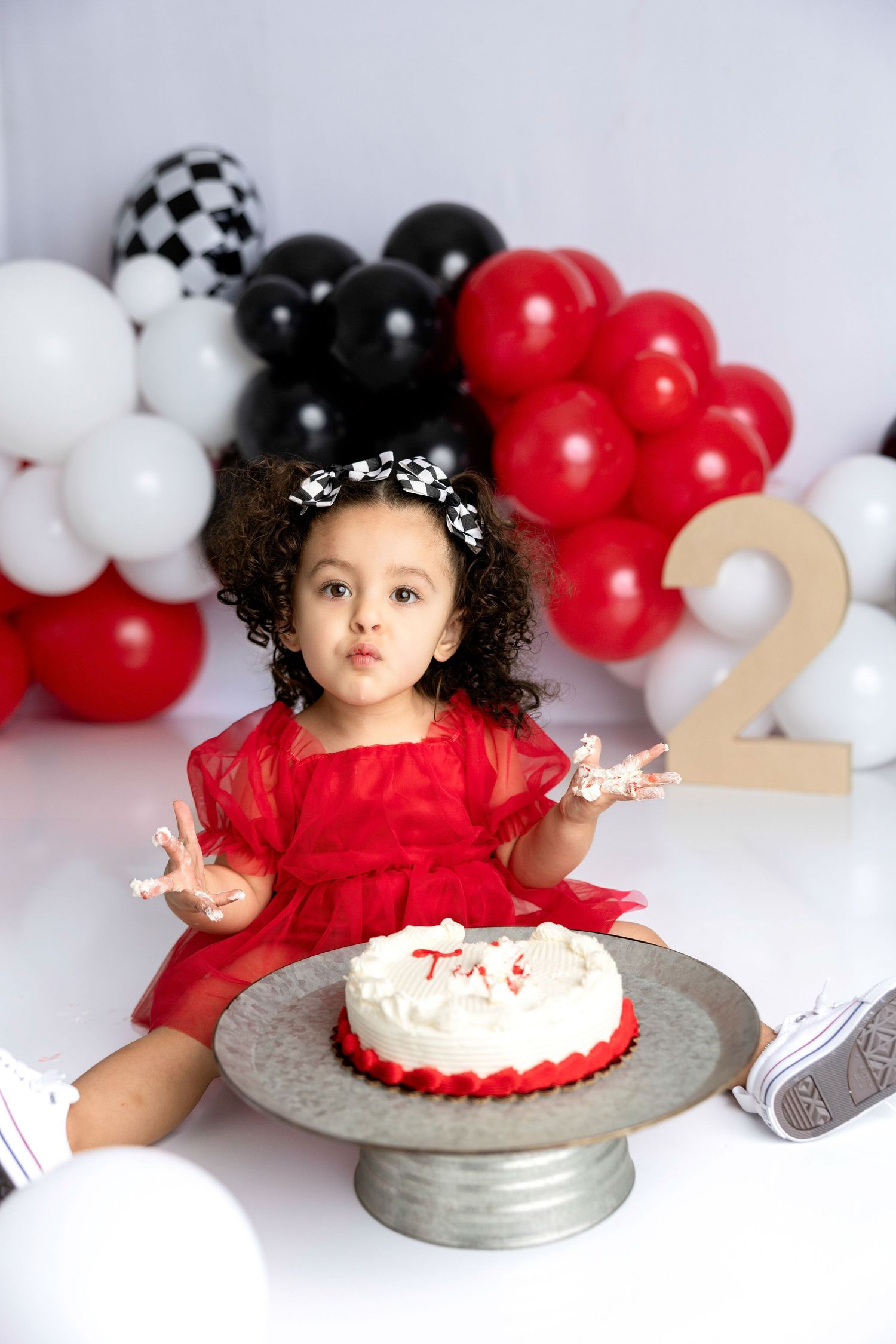 Birthday celebration setup with red, black and white balloons and cake on silver platter.