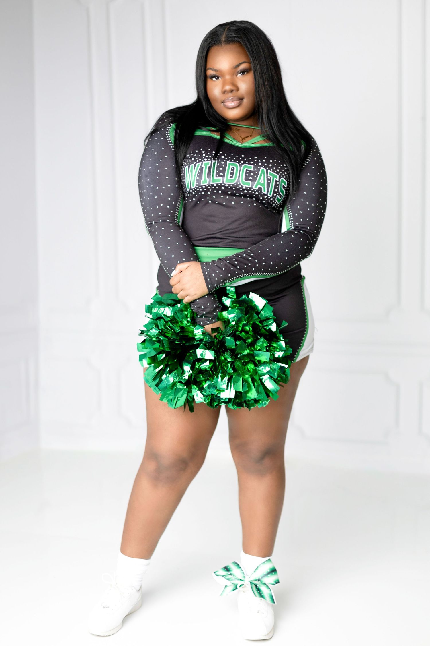 Cheerleader in black and green Wildcats uniform holding green pom poms and posing for a portrait.