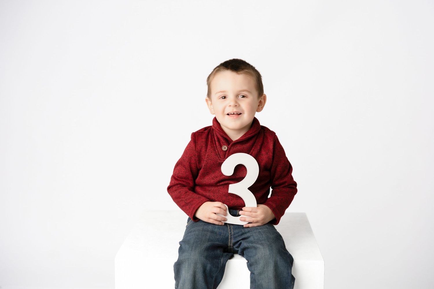 Child in red sweater sitting with number 3 against white background.