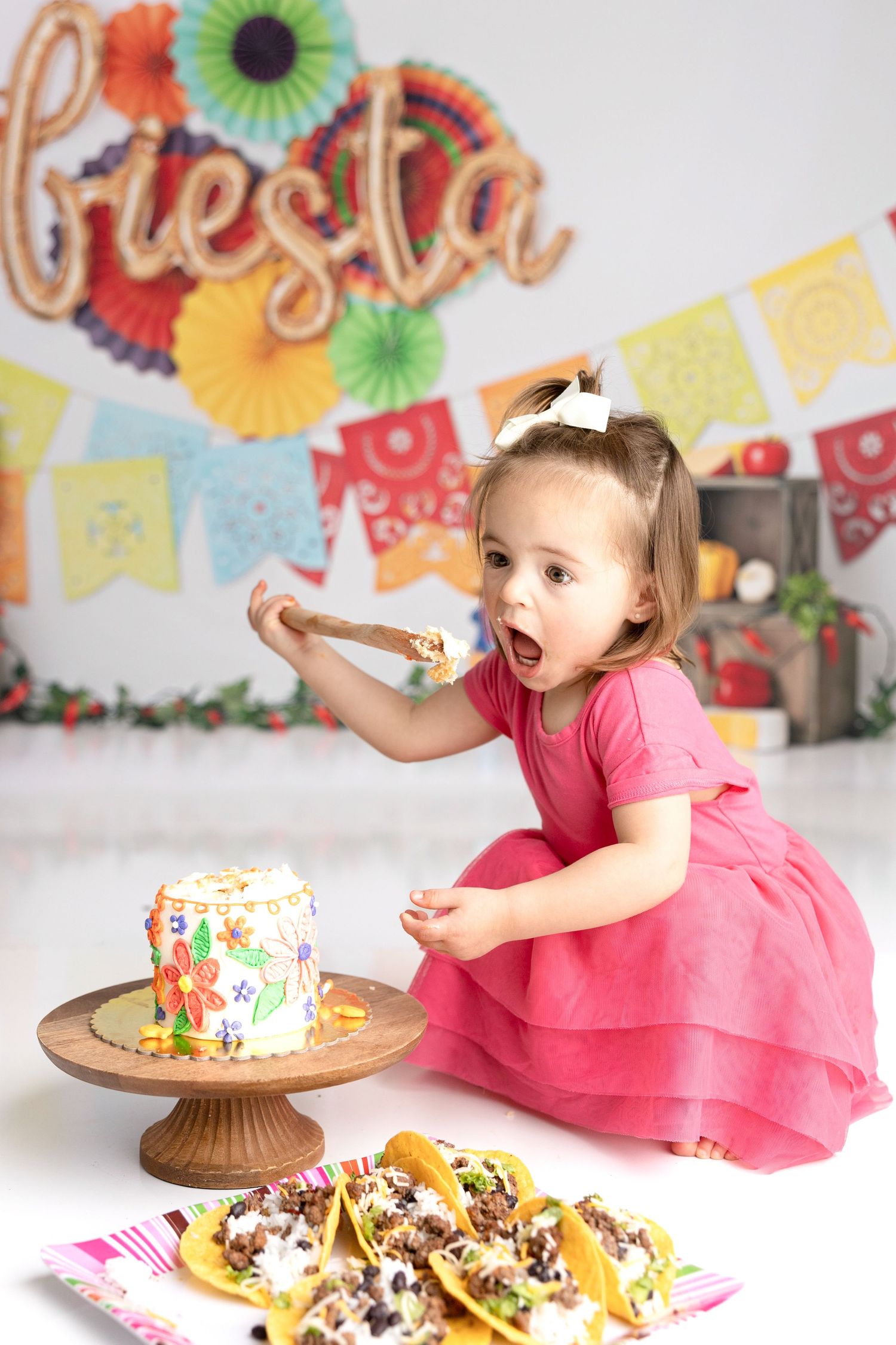 A festive cake smash photography session with colorful banners and decorations.