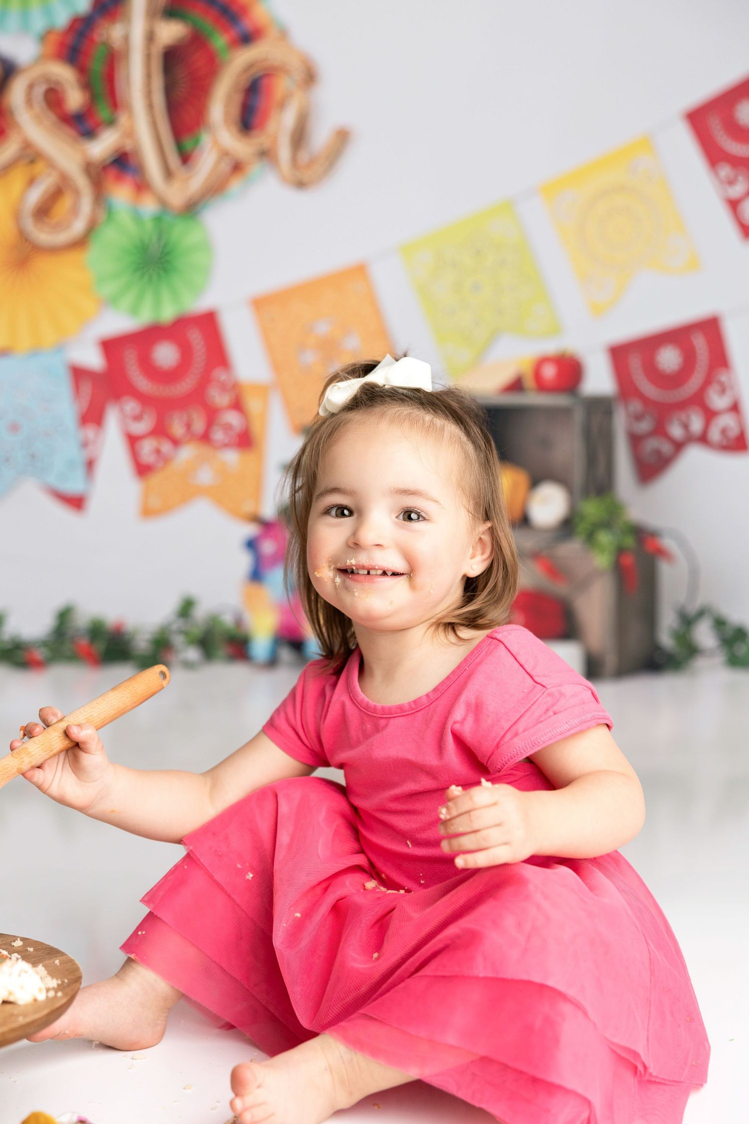 A cheerful cake smash portrait session with rainbow banners and party decorations.