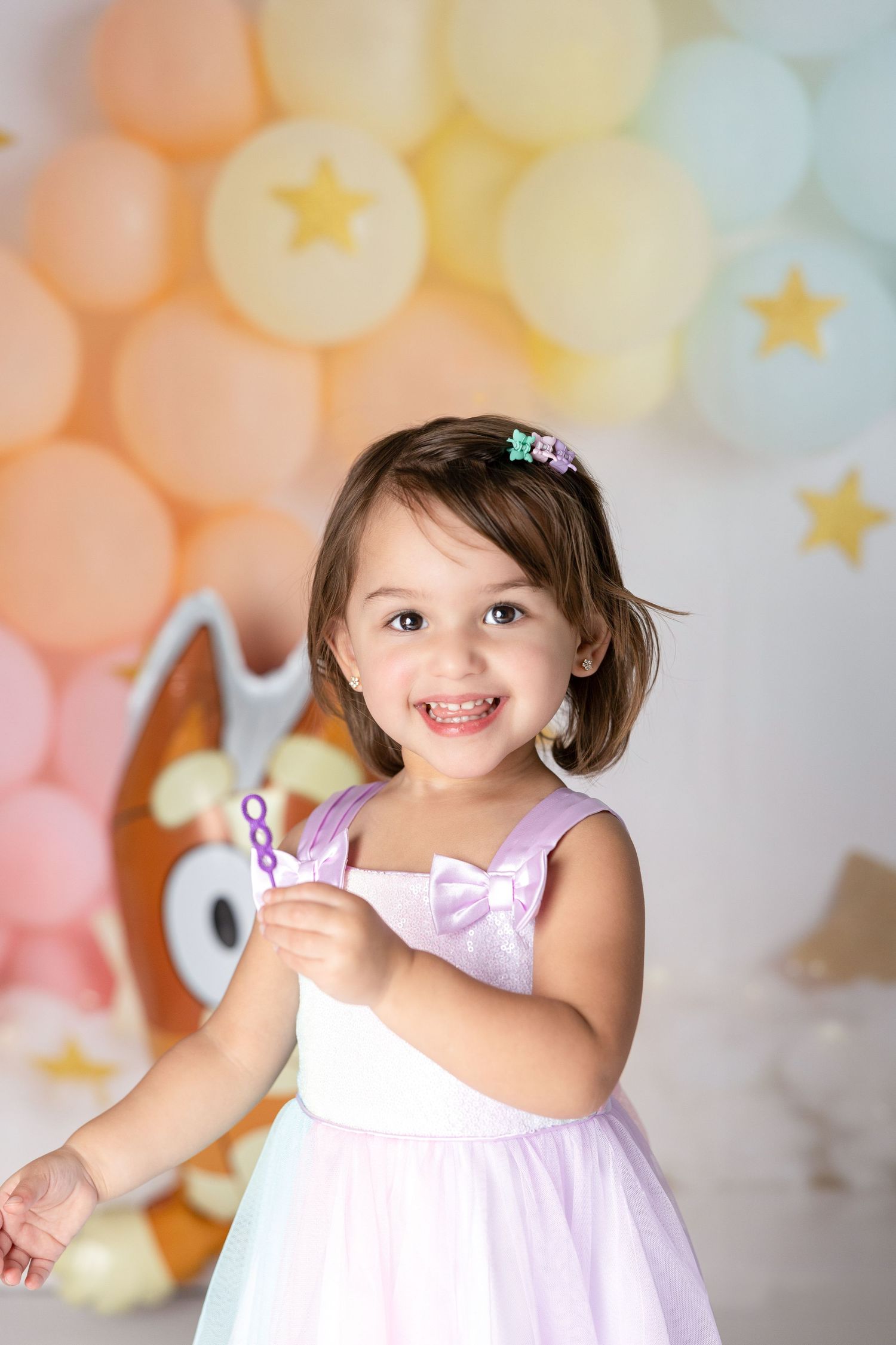 Birthday celebration scene with pastel balloon arch and soft plush toys in the background.