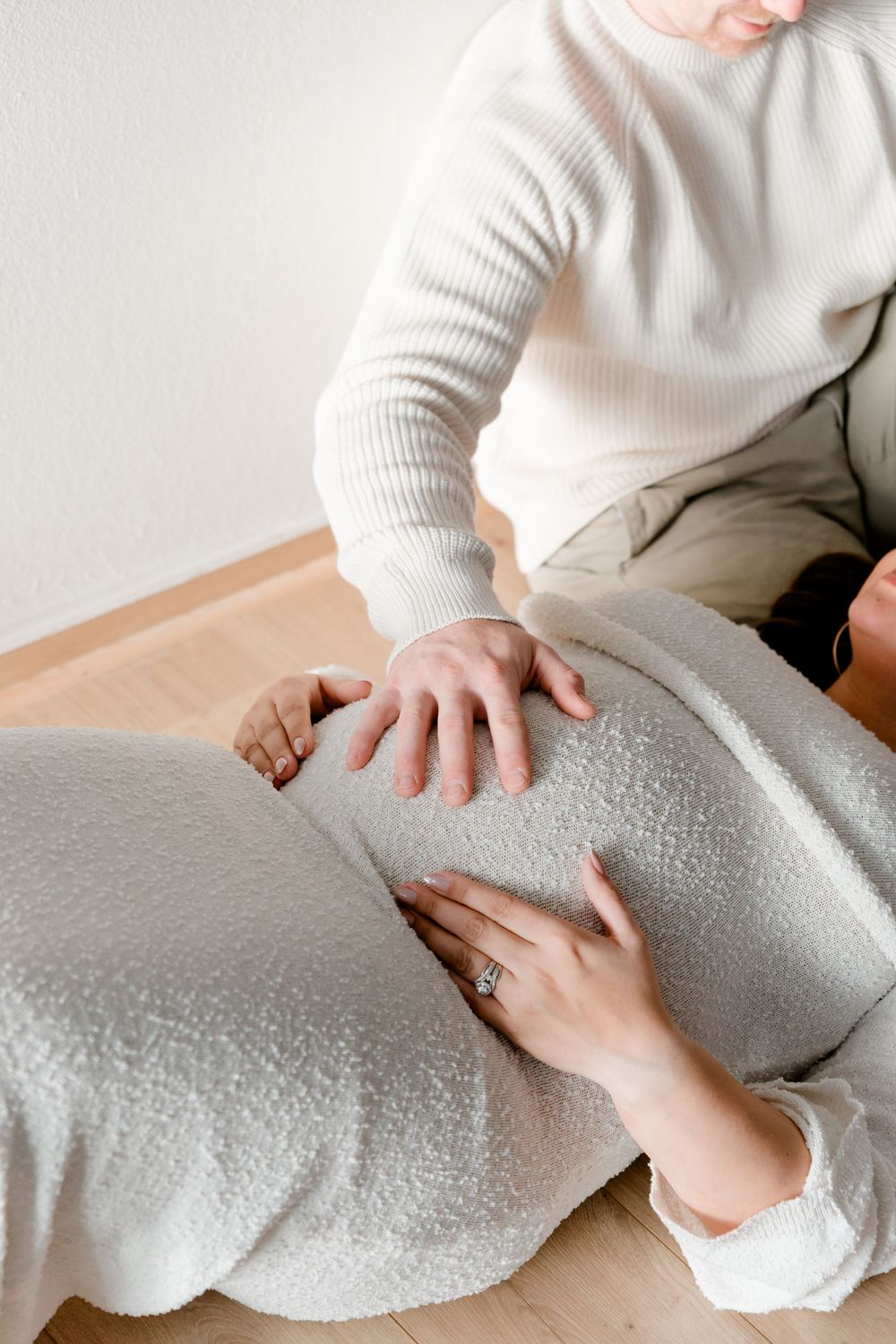 Partner placing hand on pregnant womans baby bump while she reclines during maternity session.