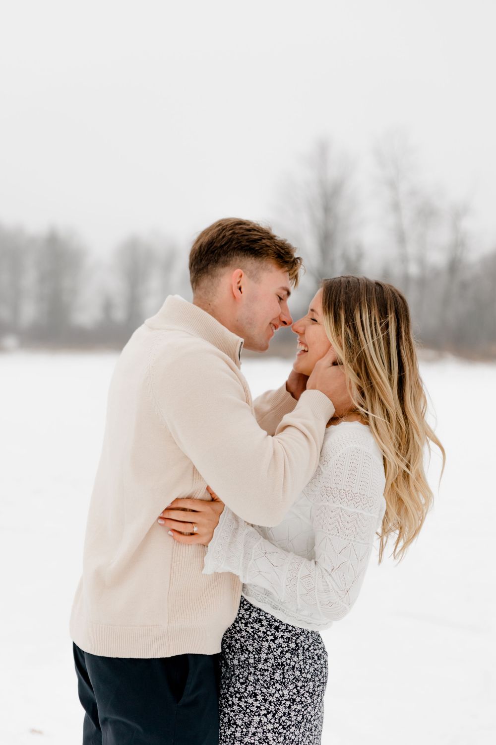 Couple sharing a romantic moment in a snowy winter landscape, both wearing cozy cream and white sweaters.