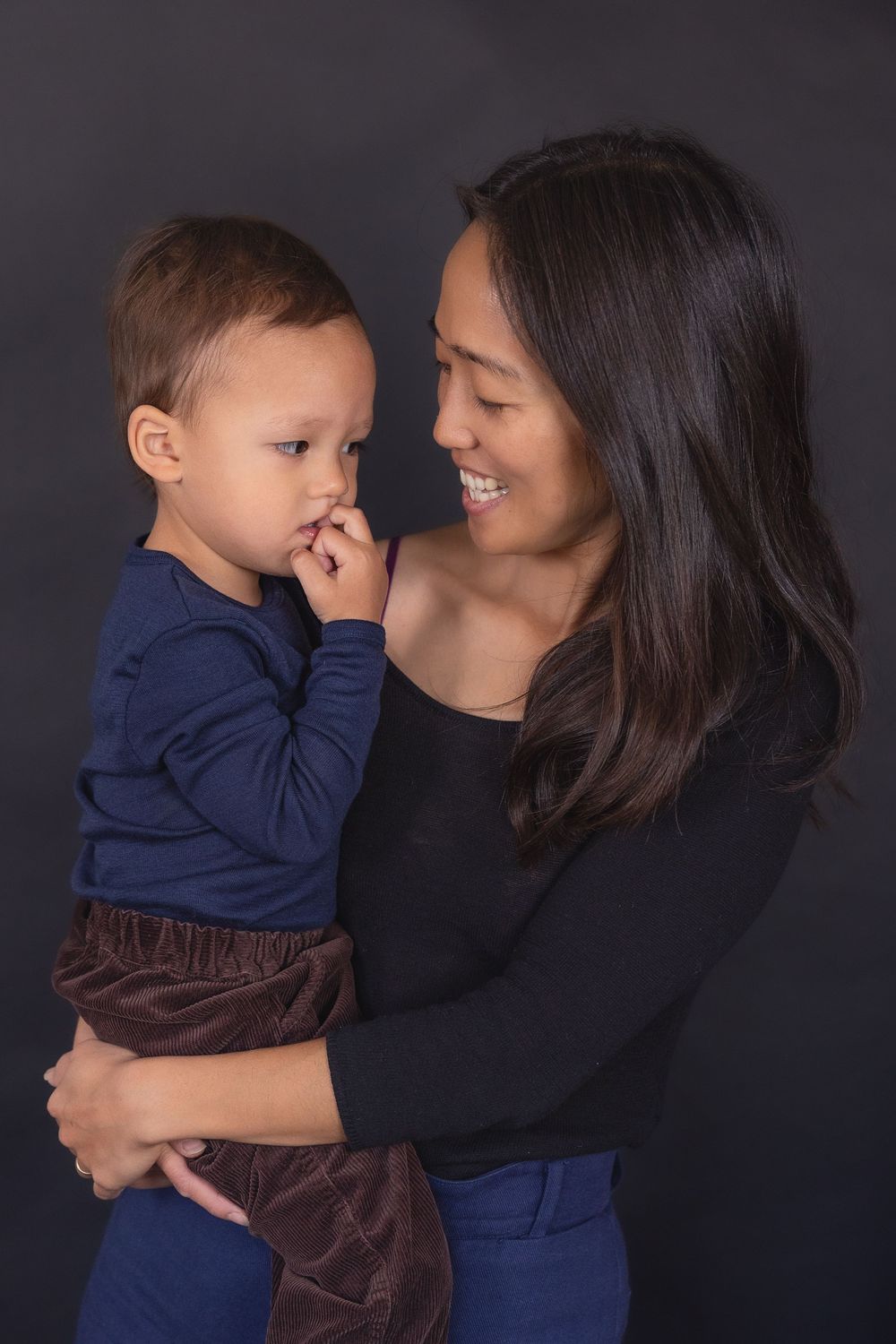 A tender moment between parent and child in matching navy blue against a dark background.