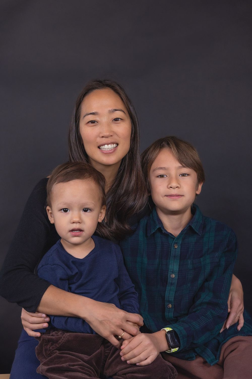 Siblings in coordinated blue outfits pose together for a casual portrait against a dark backdrop.