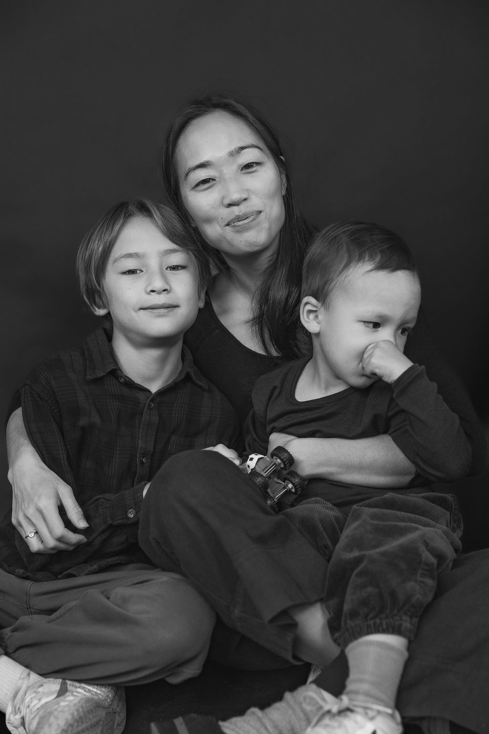 Black and white photo series showing siblings in dark clothing cuddling and playing together on a couch.
