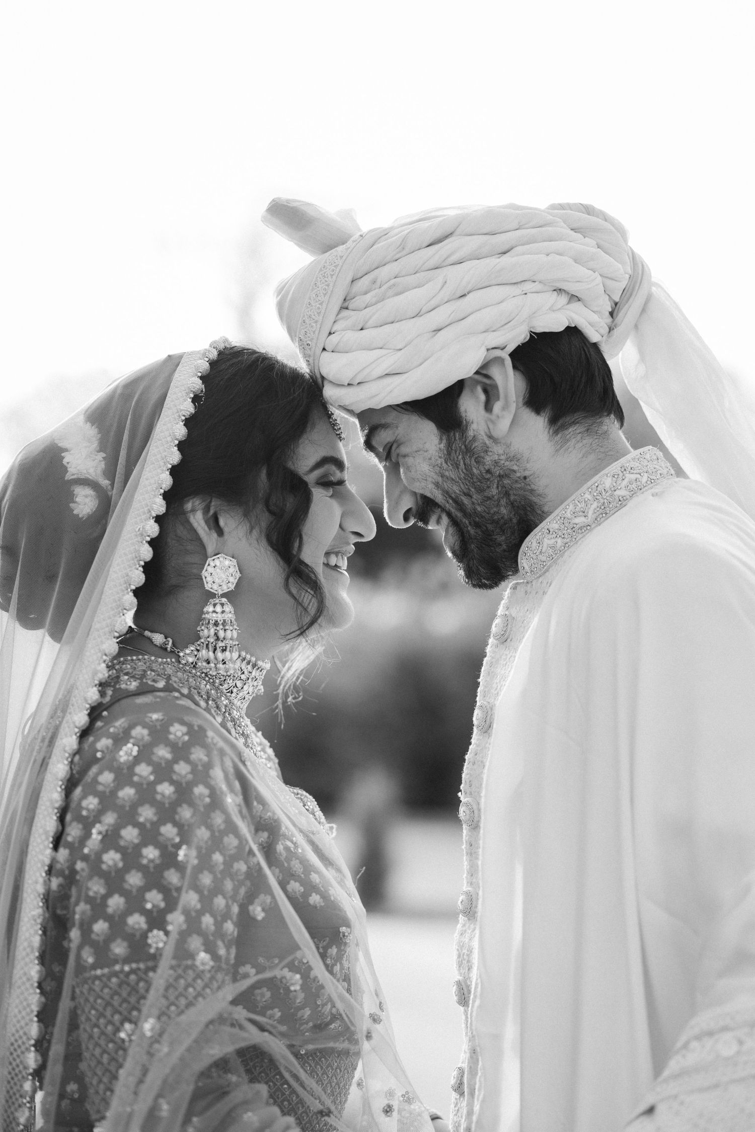 Black and white wedding photo showing couple in traditional South Asian attire sharing intimate moment.