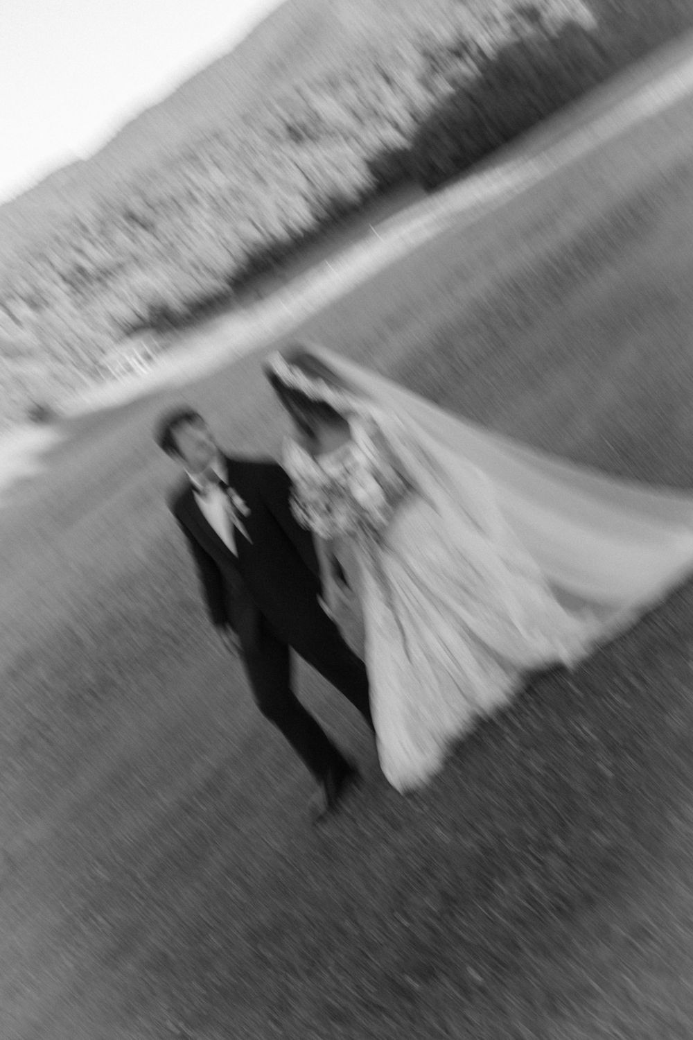 Black and white aerial photo of bride and groom walking outdoors on their wedding day, with motion blur effect.