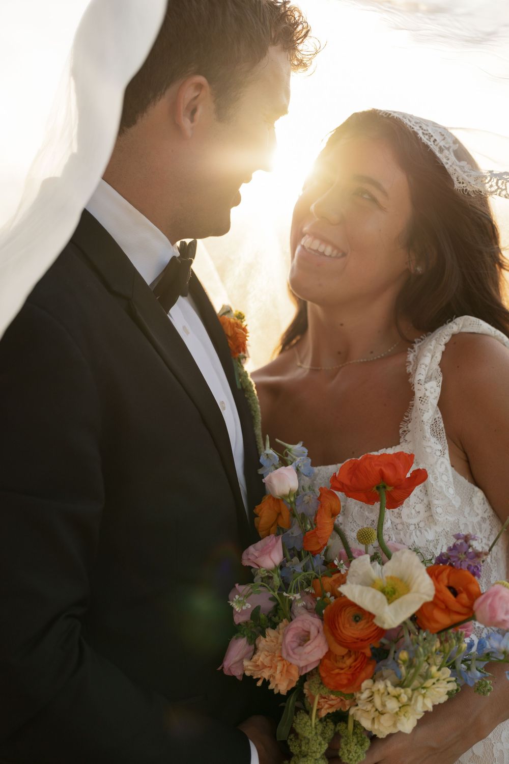 Bride and groom share a romantic moment at golden hour, bride holding a colorful bouquet of roses and wildflowers.