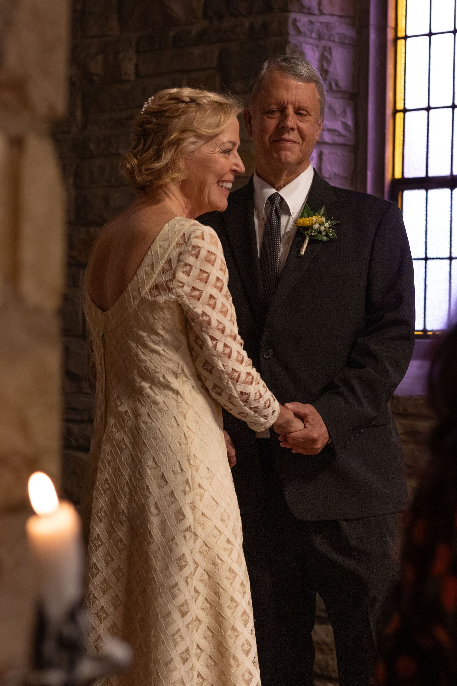 Couple dancing in candlelit stone chapel interior with stained glass windows.