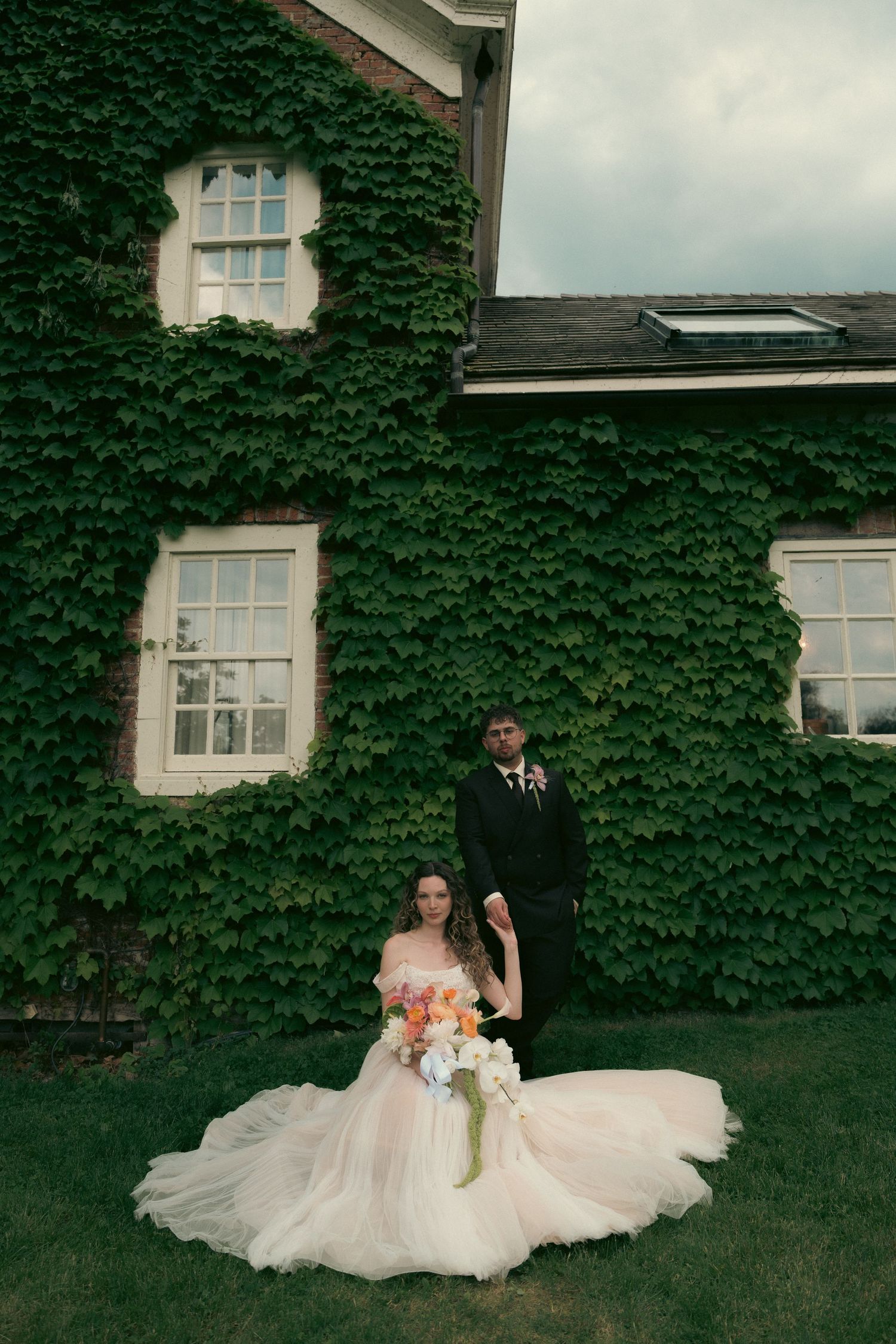 A couple walks hand in hand across a scenic grassy field on their wedding day at sunset.