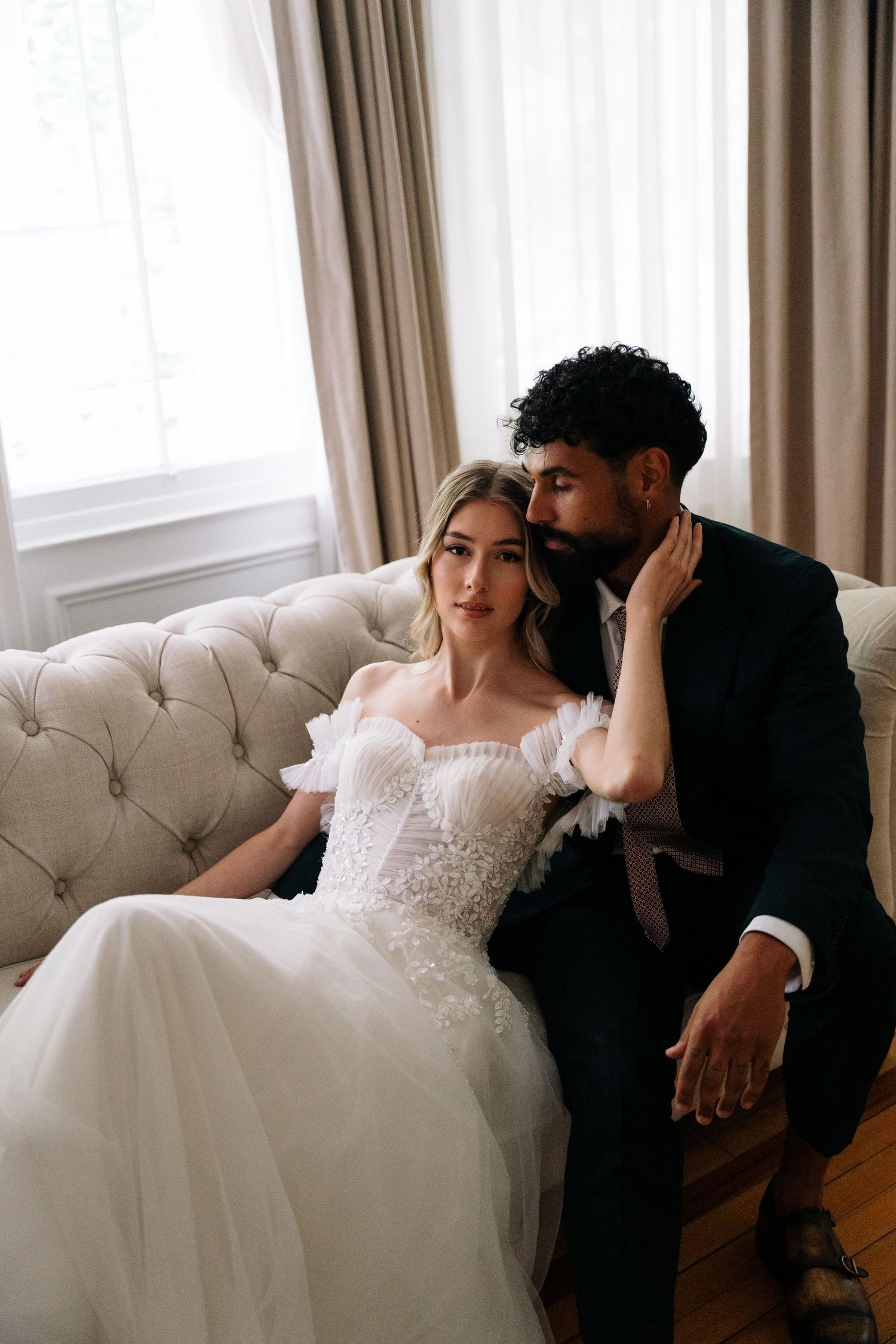 A romantic wedding portrait on an elegant tufted sofa with soft window light.