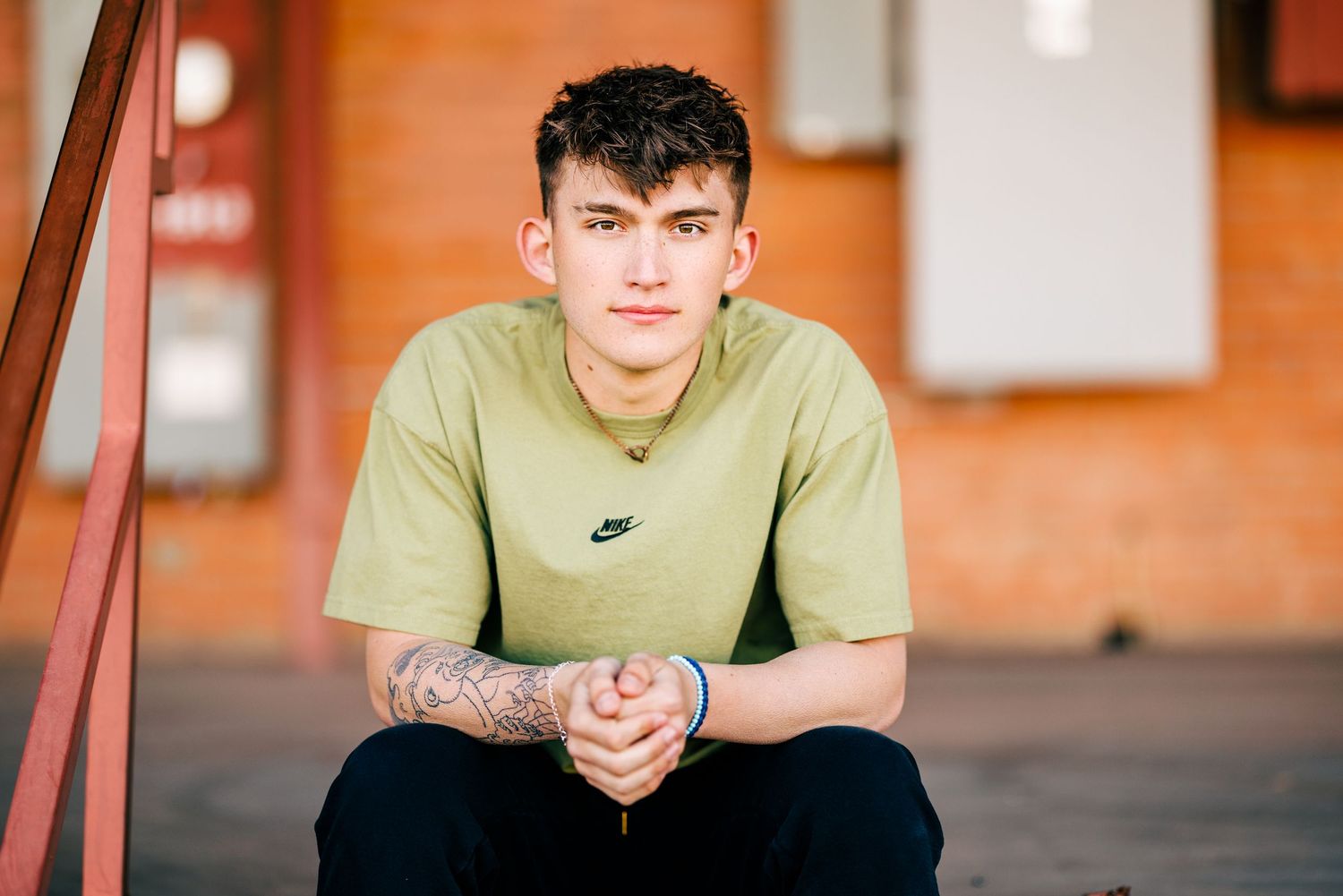 A casual portrait of someone wearing a green Nike t-shirt sitting on outdoor stairs.