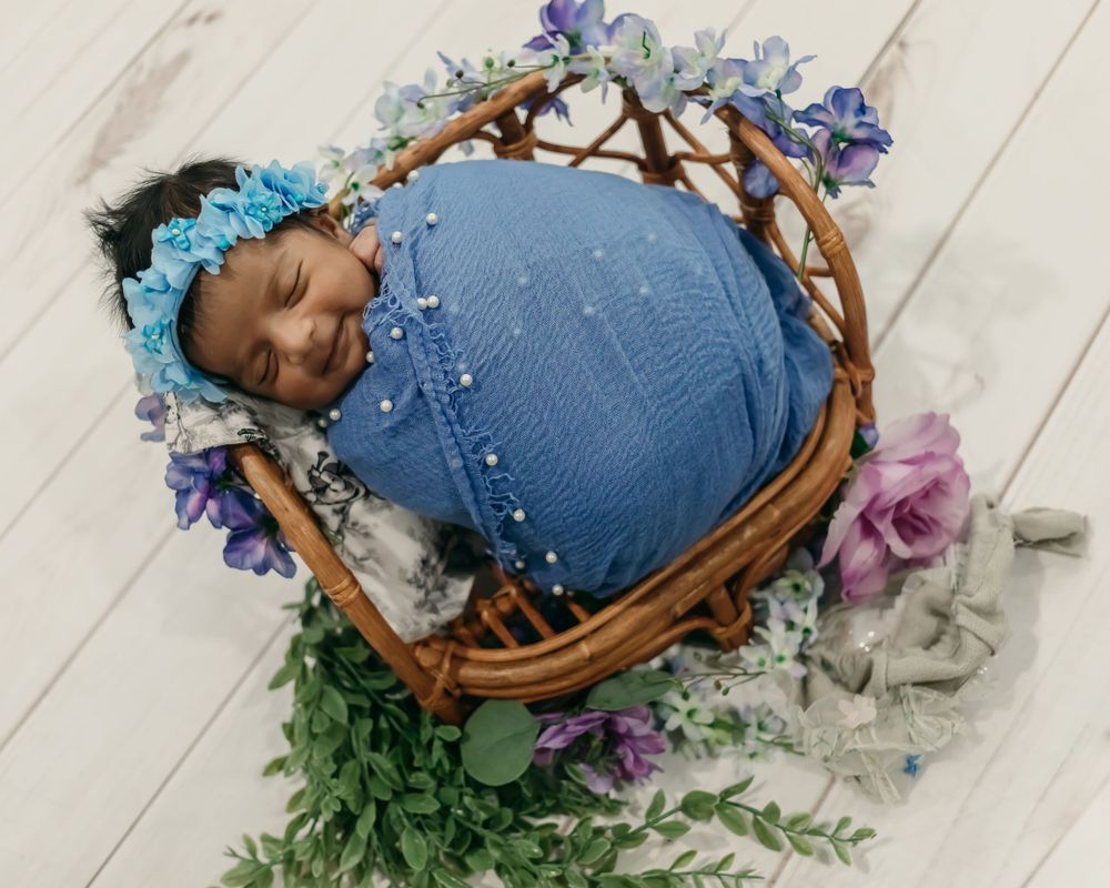 Baby sleeping in wicker basket decorated with blue flowers and pearls.