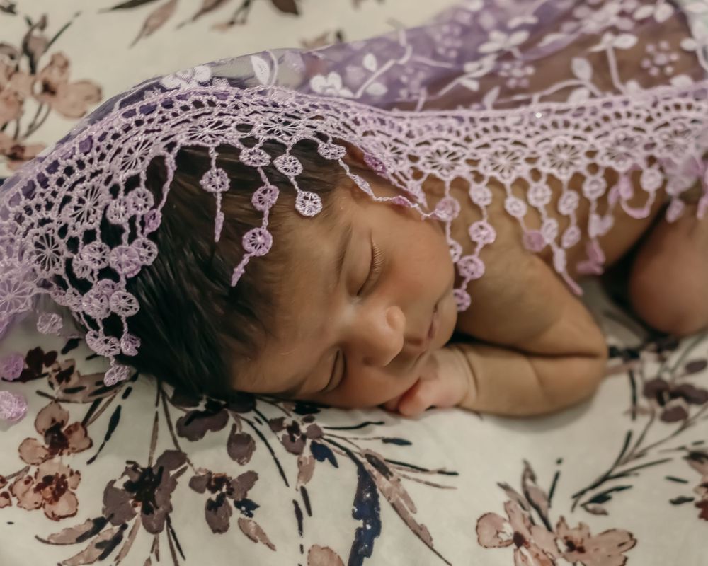 Sleeping newborn with delicate pink lace overlay in a dreamy portrait setting.