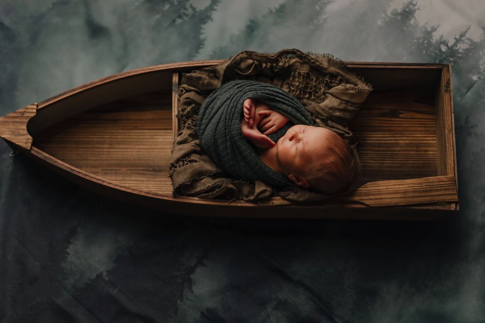 Artistic overhead view of sleeping infant in wooden boat set against dark backdrop.