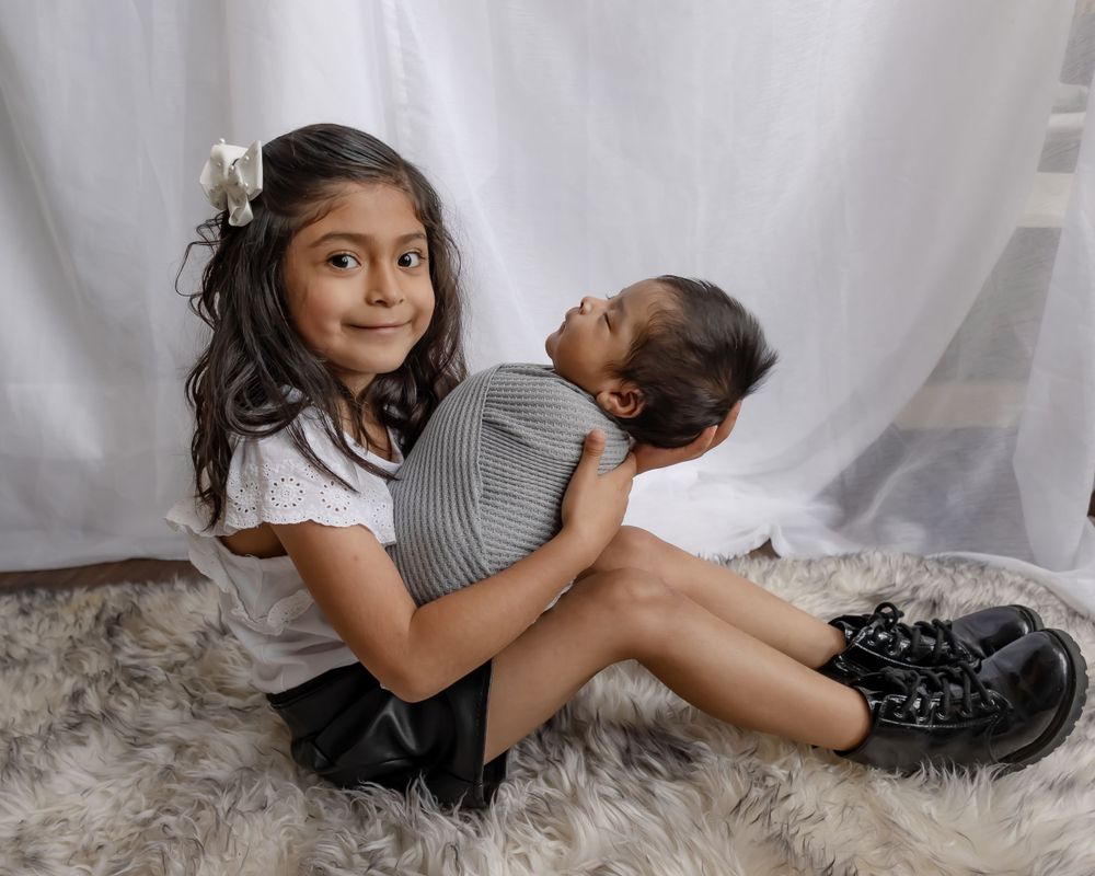 Two siblings in a portrait studio setting on a furry rug against white backdrop.