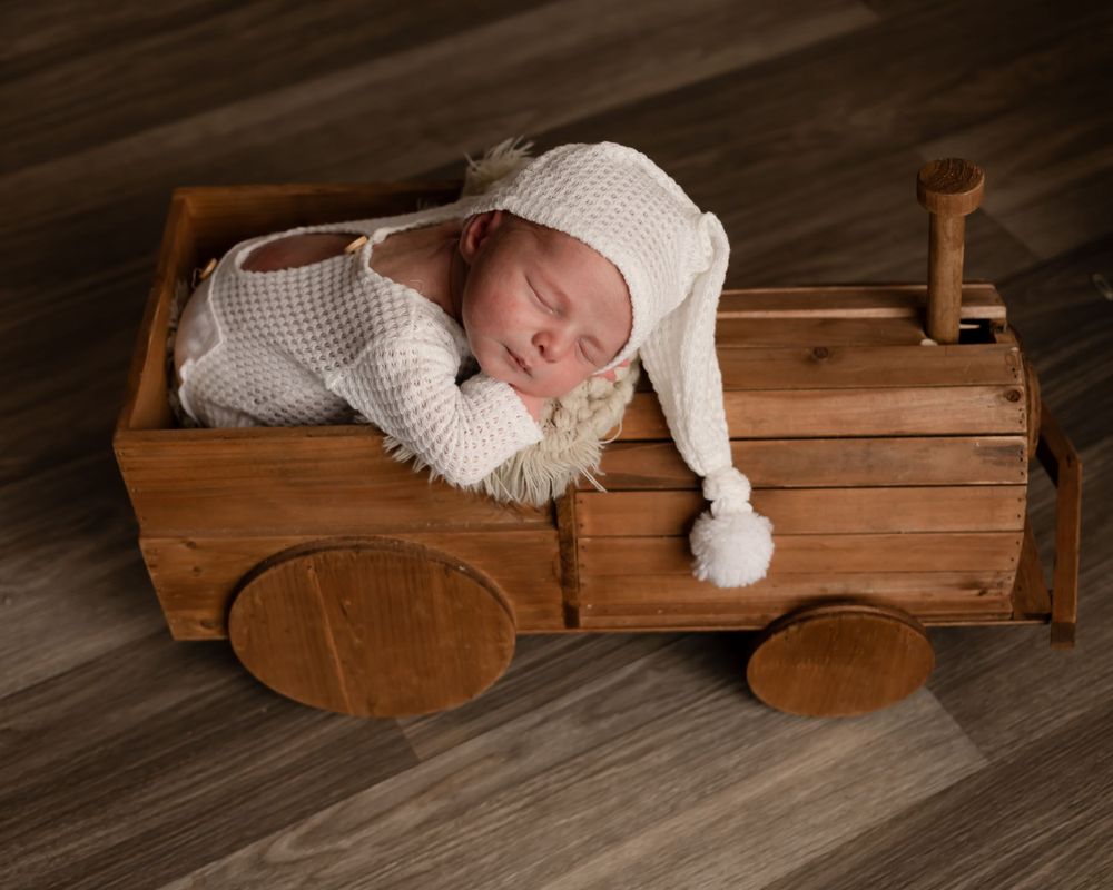 Baby sleeping in wooden toy wagon wearing white knit outfit.