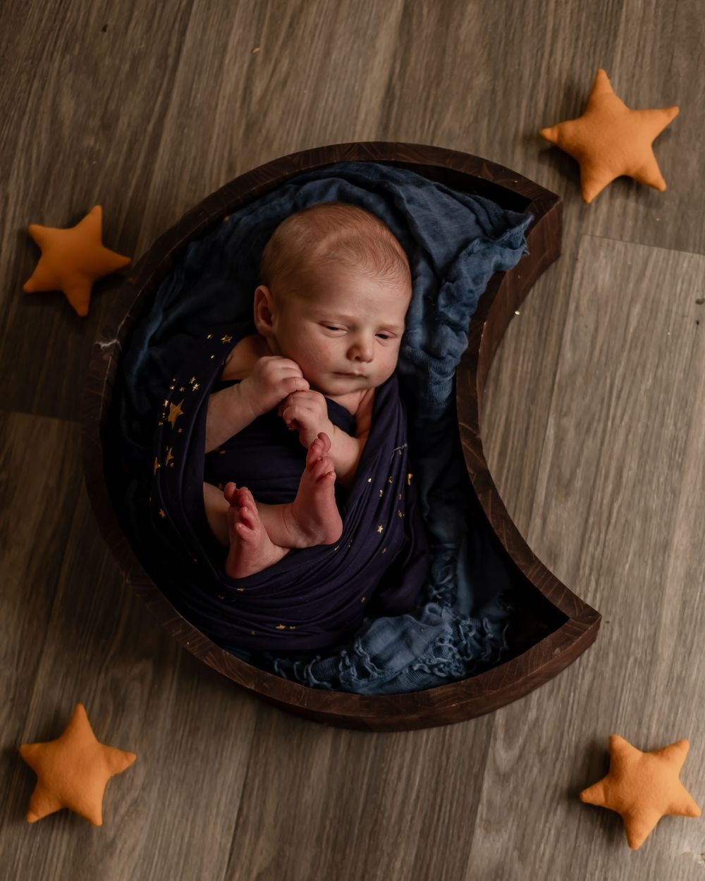 Baby sleeping in crescent moon-shaped prop with orange star decorations.