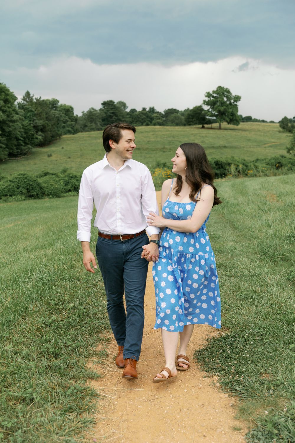 A couple in casual attire shares a romantic moment while walking on a nature trail.